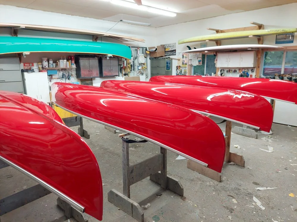 Multiple canoe hulls in red and turquoise in a workshop.
