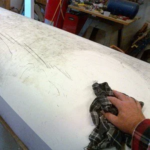 A person cleaning a white surfboard with a cloth in a workshop.