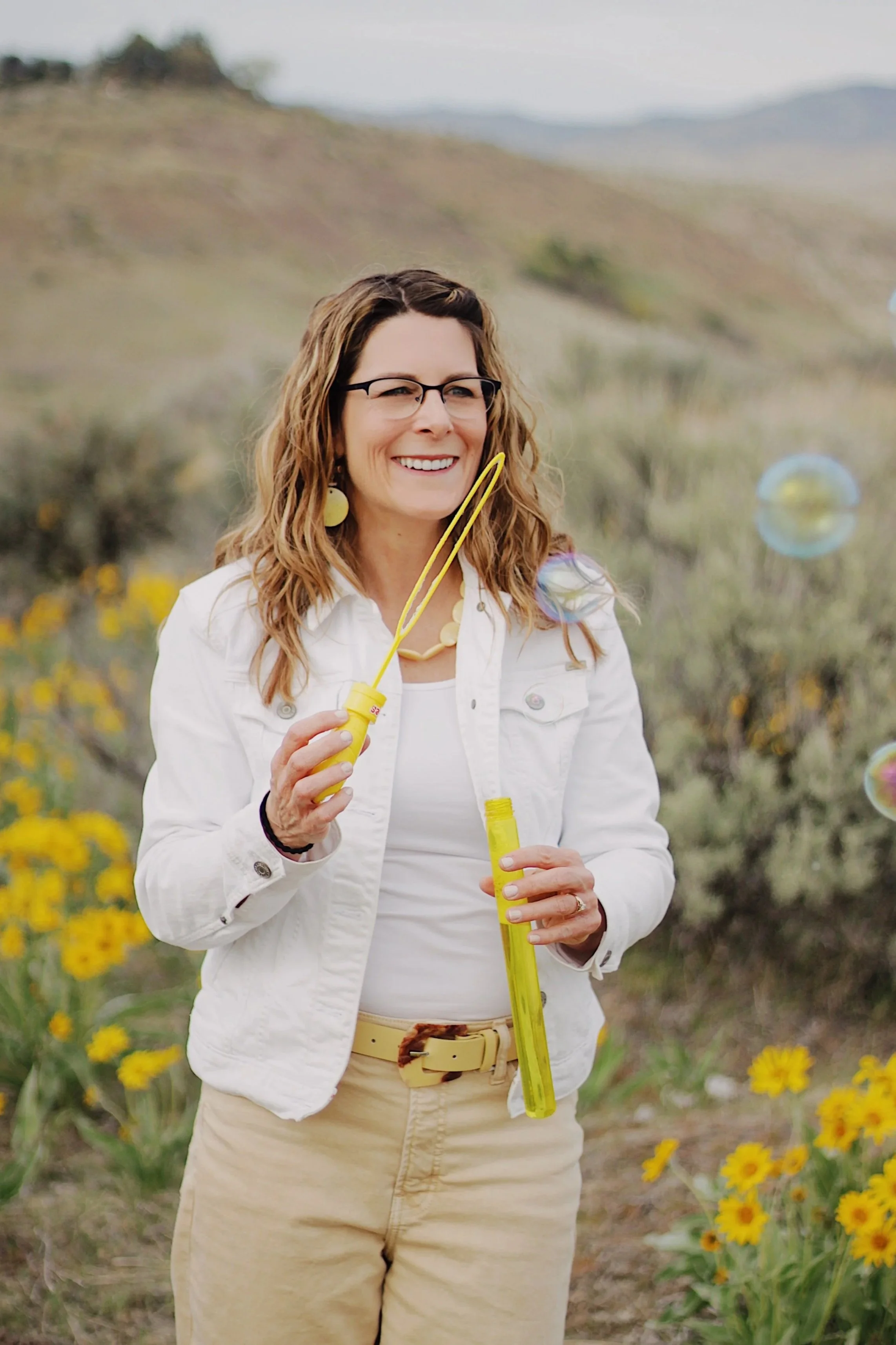 Michelle Batten LPC trauma therapist Boise Idaho blowing bubbles in yellow wildflower field