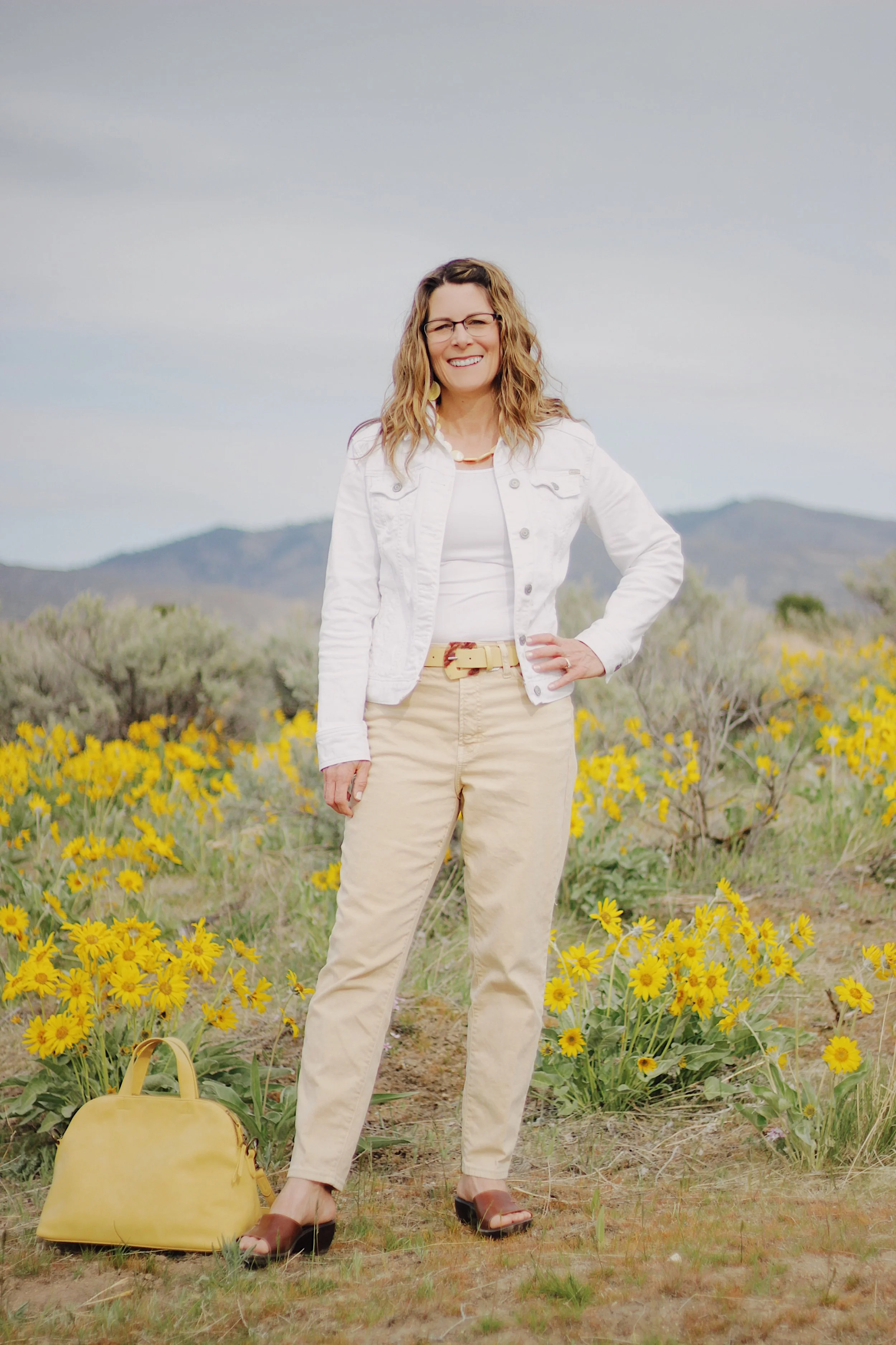 Michelle Batten LPC standing in yellow wildflower field Boise Idaho with yellow handbag