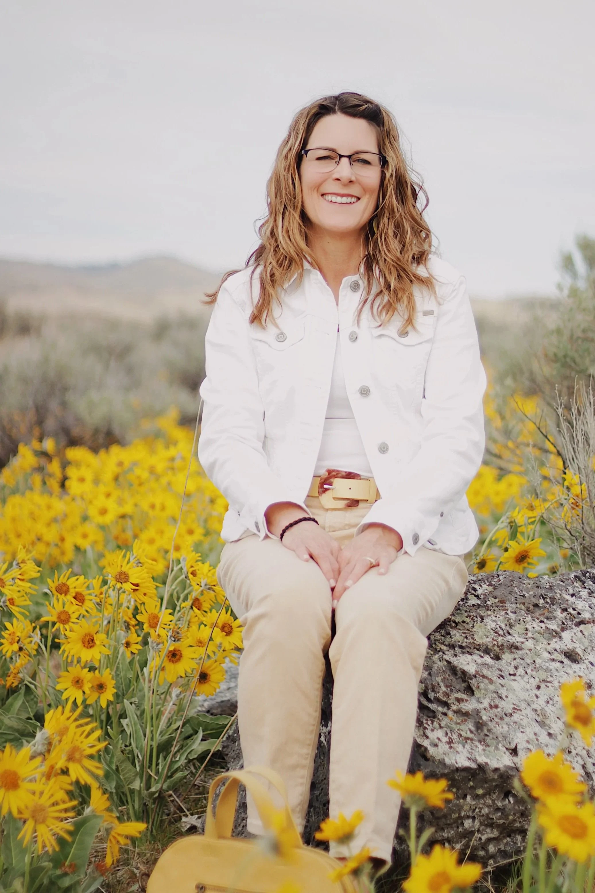 Michelle Batten therapist sitting on rock surrounded by yellow wildflowers in Boise Idaho