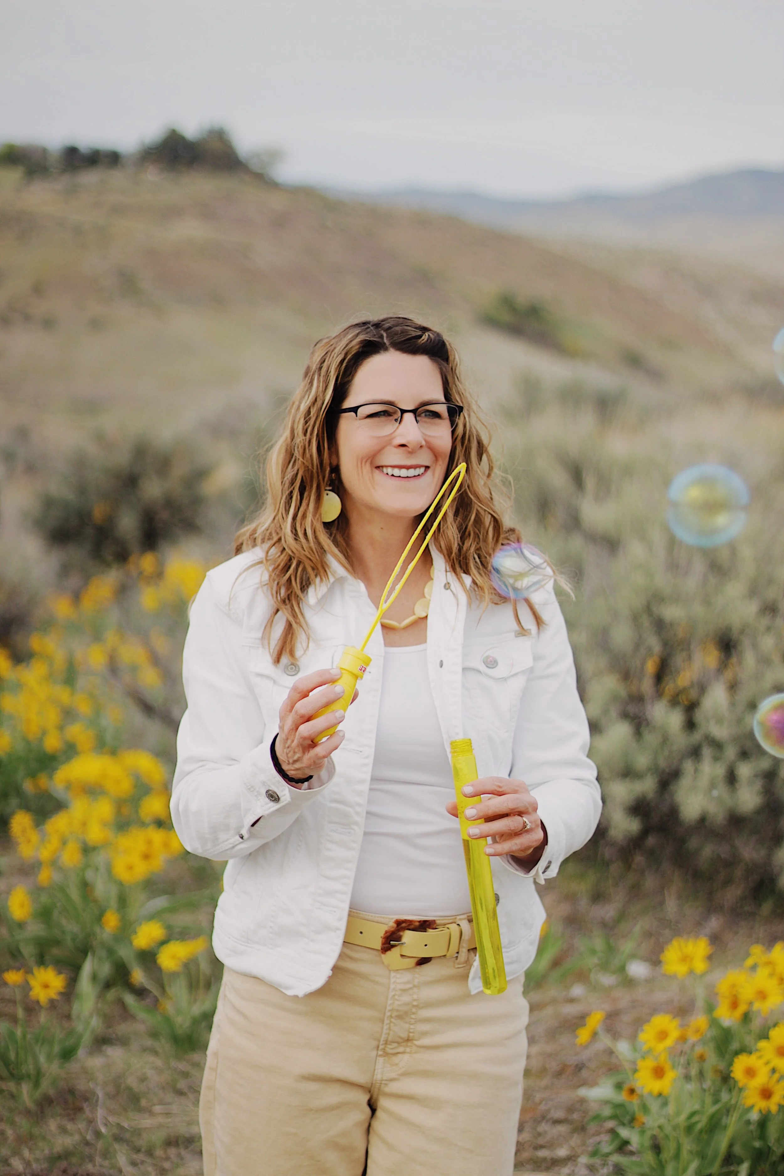 Michelle Batten LPC trauma therapist Boise Idaho blowing bubbles in yellow wildflower field