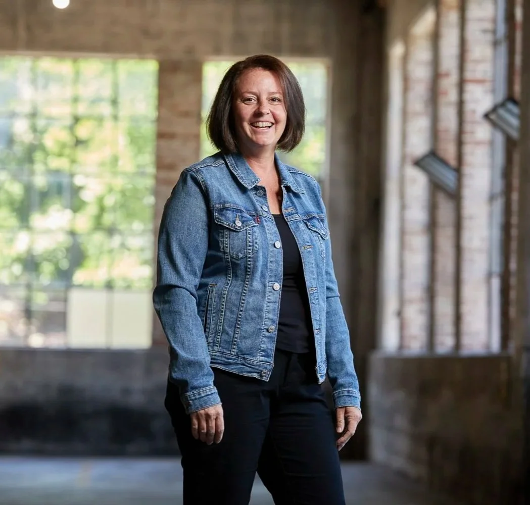 Erin Rue, a confident and inspiring small business tax accountant, smiles warmly in a relaxed denim jacket against a bright, airy backdrop, showcasing her authentic approach to navigating taxes.