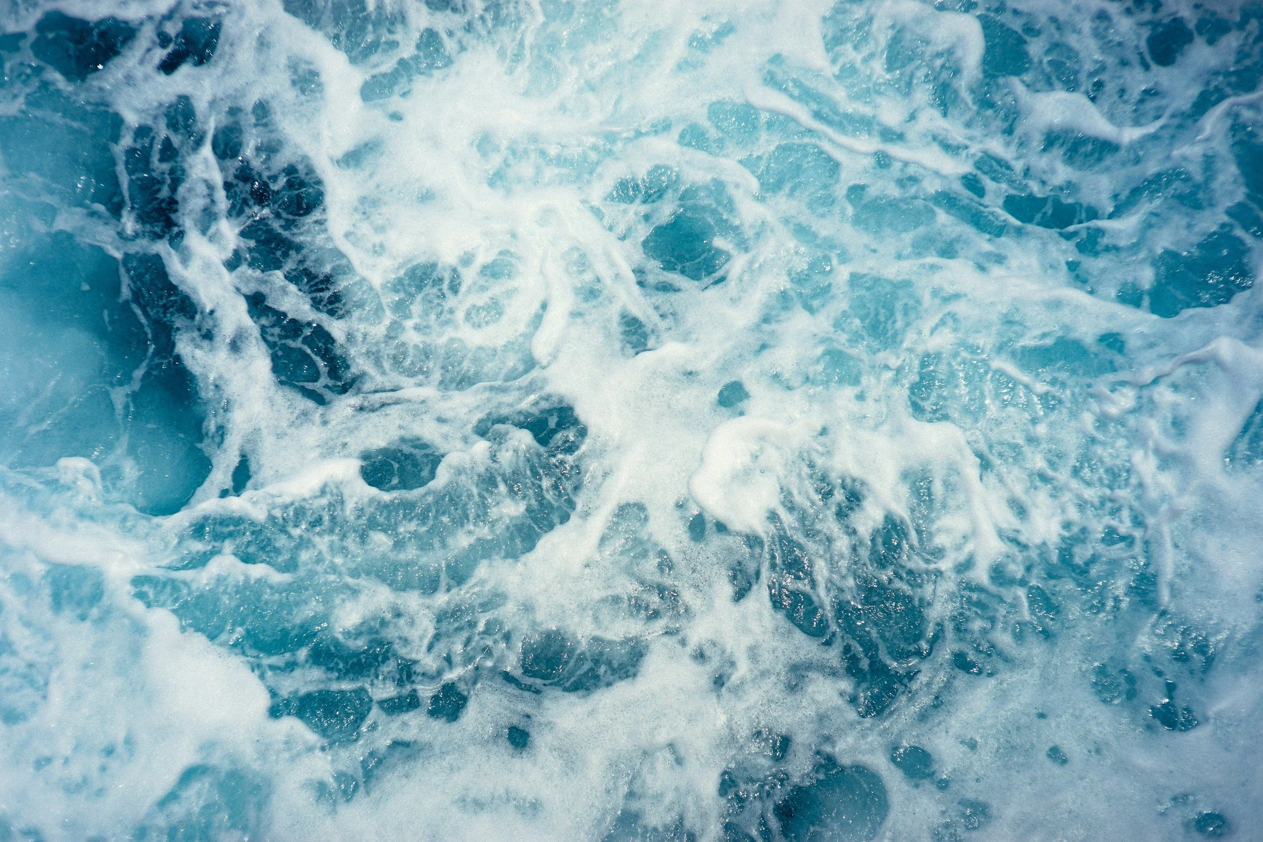 Close-up of swirling foamy ocean waves in bright blue water.