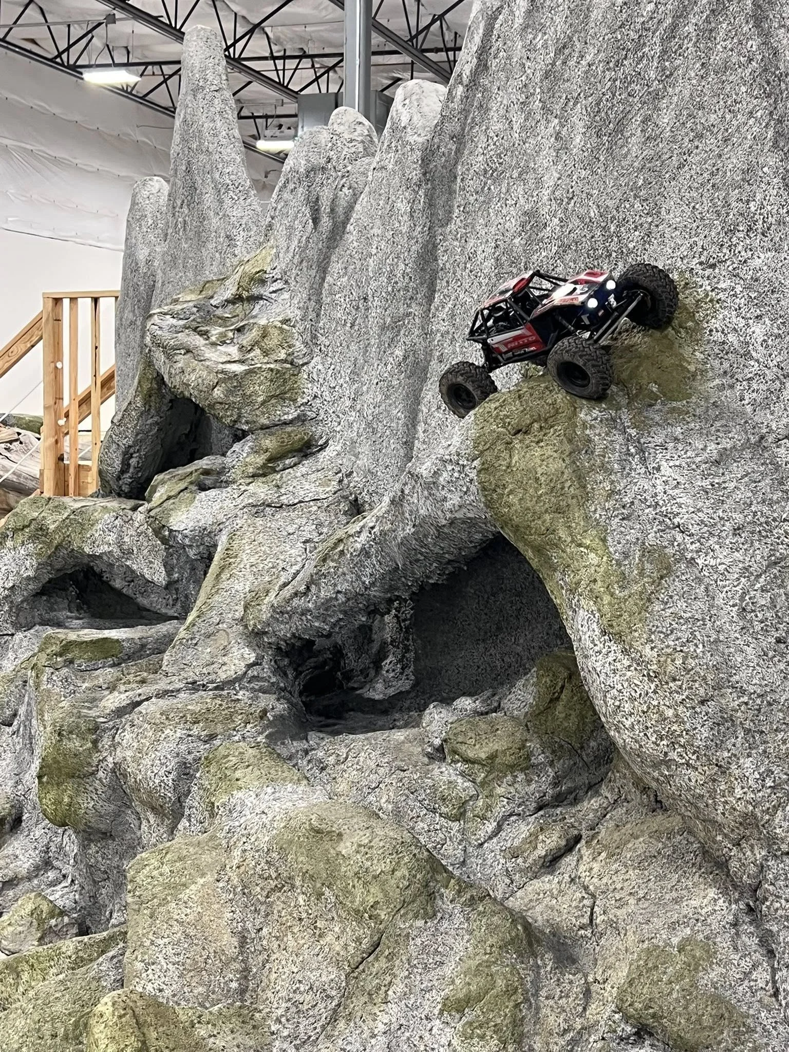 A remote control car climbing a rock wall at an indoor recreational facility.