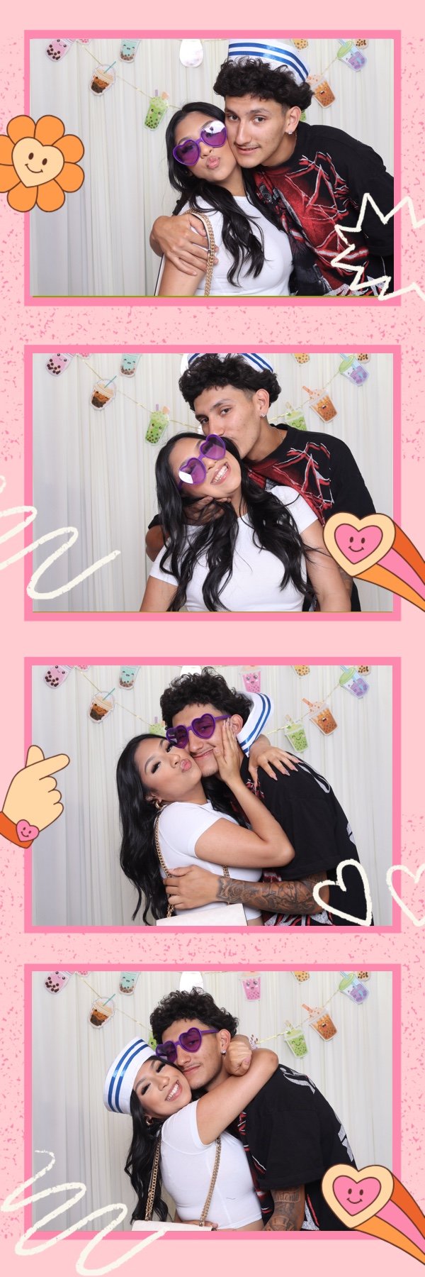 A young couple celebrating with photos in a photo booth at a festive party. The woman is wearing heart-shaped purple sunglasses and a white top, and the man is wearing a sailor hat, black shirt with red designs, and purple heart-shaped sunglasses. Th