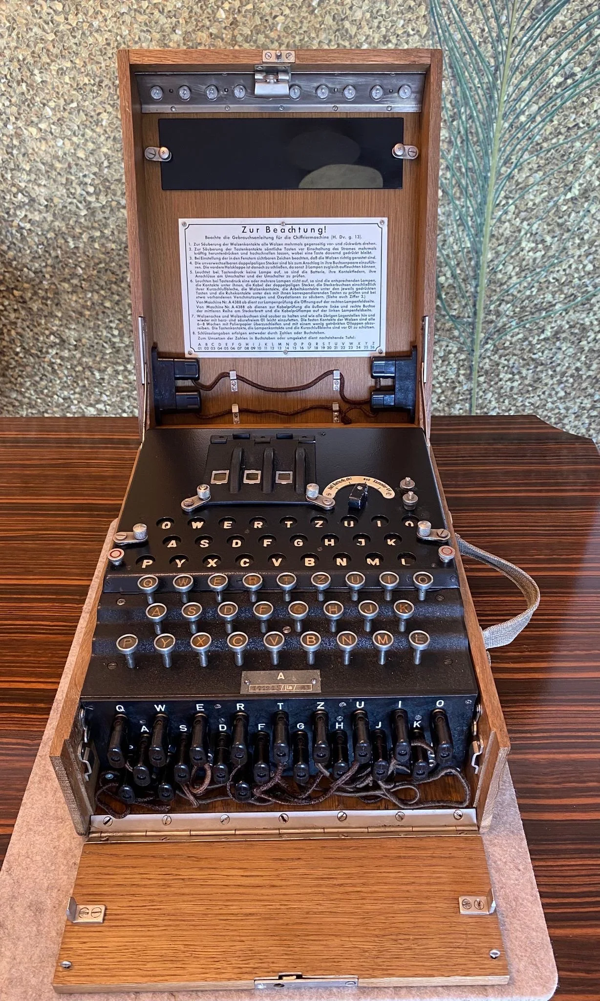 A vintage German Enigma cipher machine with a wooden case and a European QWERTZ keyboard, resting on a wooden surface.
