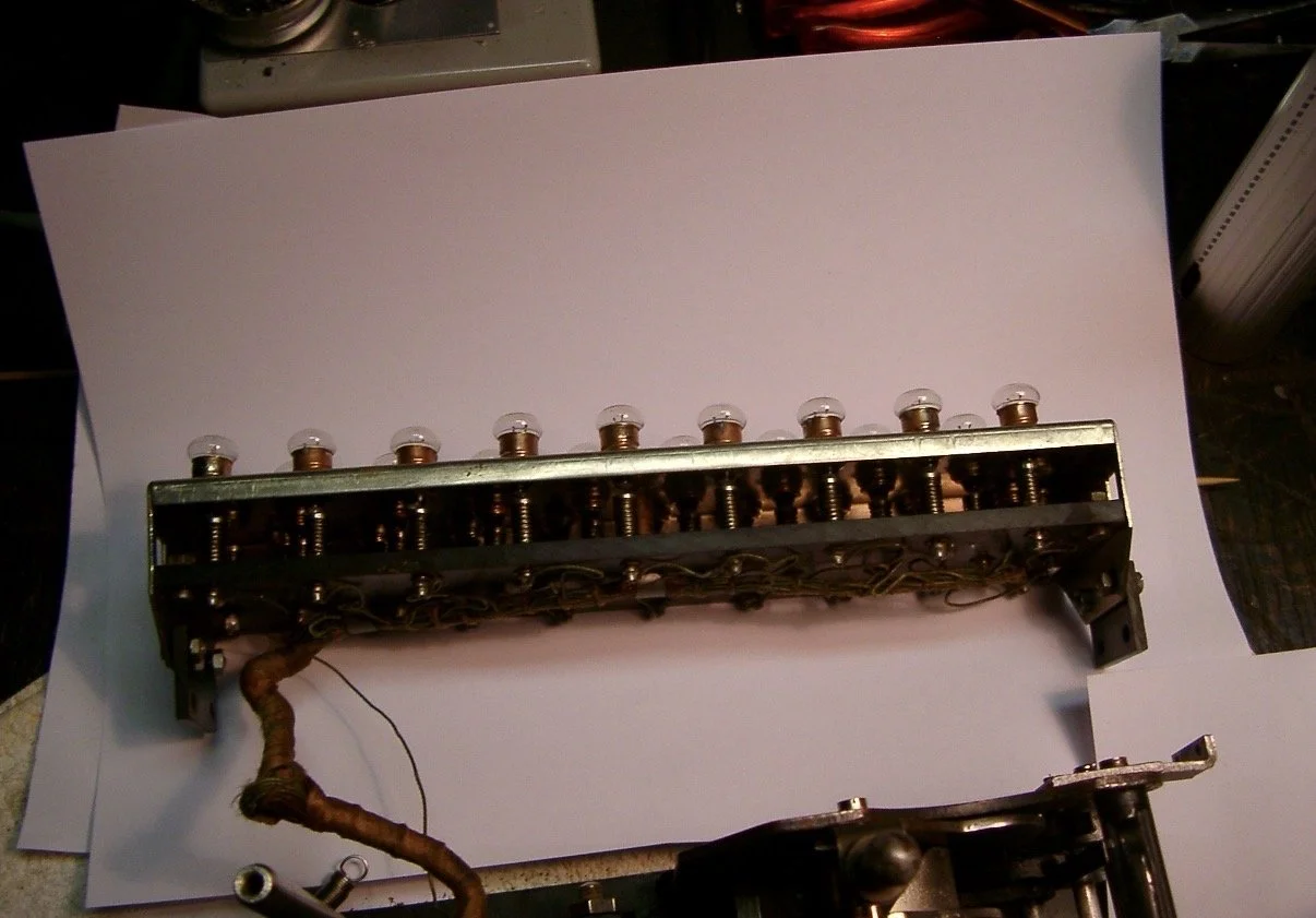 A metal mechanical part with multiple small glass bulbs on top, connected by copper wires, resting on white paper.