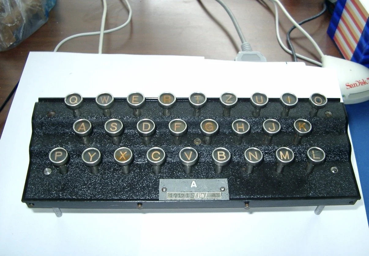 A vintage typewriter with round keys on a black textured metal base, sitting on a white surface.