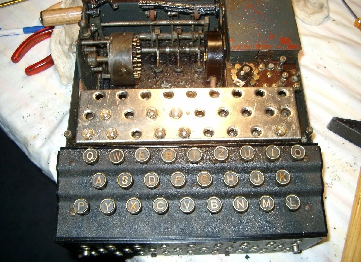 An old enigma machine with black keys and a metal body, showing its internal components and partially disassembled parts.