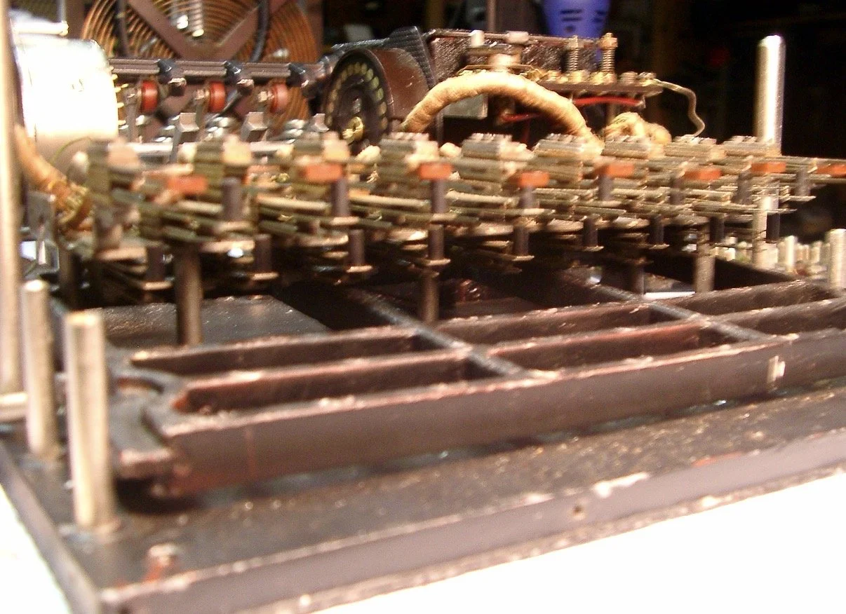 Close-up of vintage mechanical device with levers, gears, and metal components, likely an old typewriter or a piece of machinery.