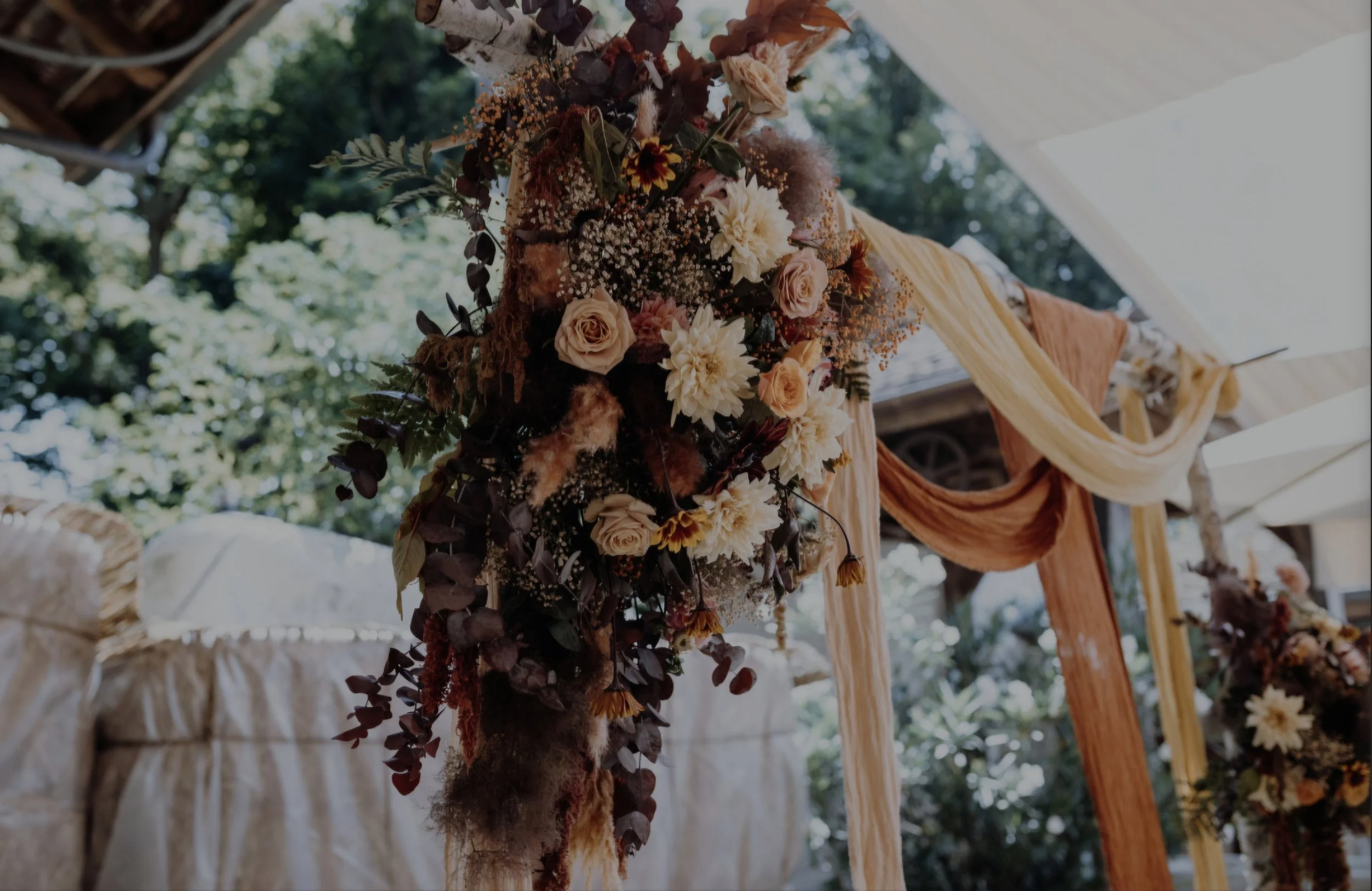 Blumenarrangement mit weißen und rosafarbenen Rosen, gelben Dahlien, Babypuderfarbenen Steppke, Beeren und grünen Blättern, auf einer Holzstange bei einer Hochzeit im Freien