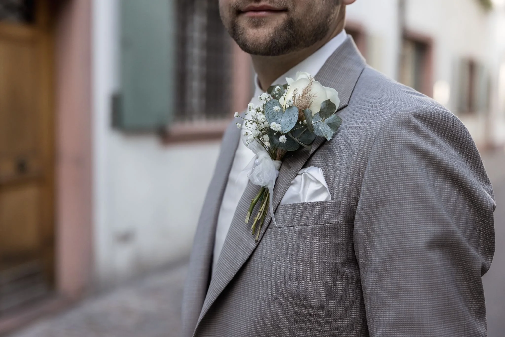 Ein Mann trägt einen grauen Anzug mit einer weißen Blume als Boutonniere am Revers.