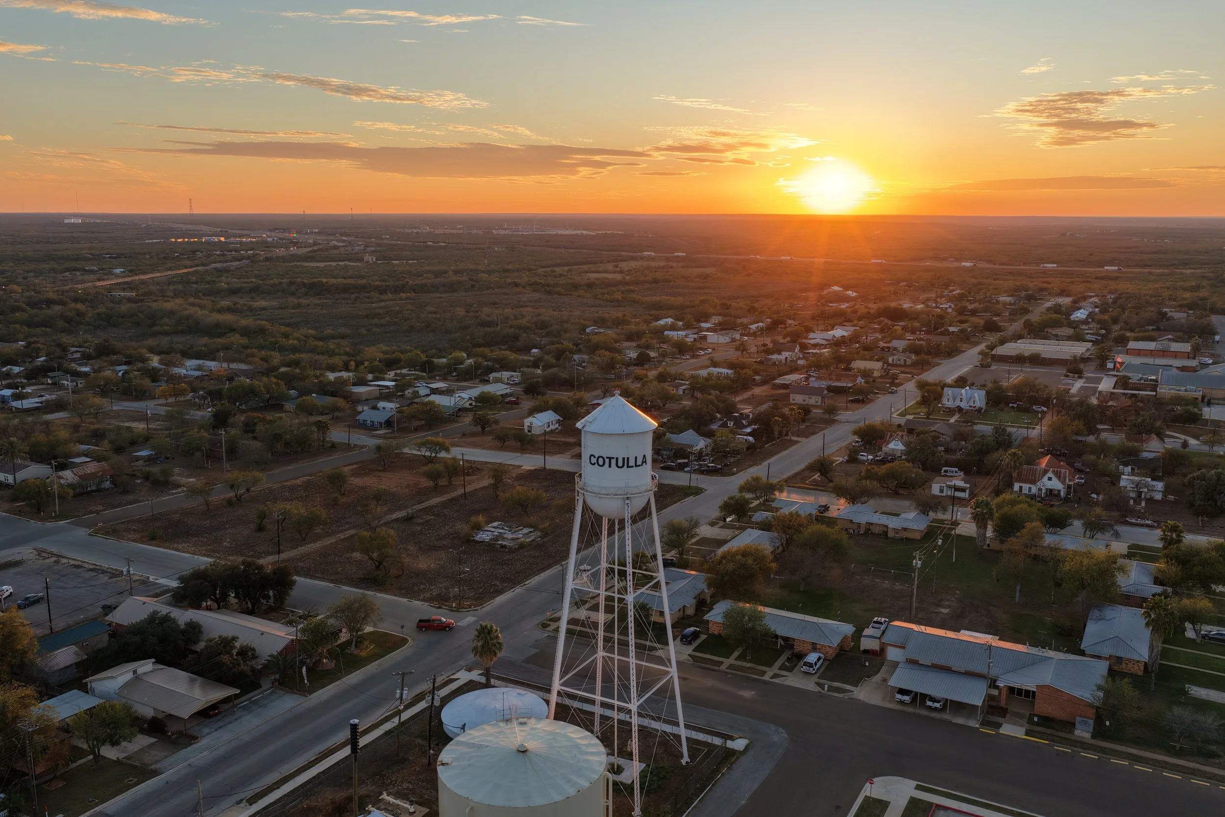 Aerial view of Cotulla town at sunset, featuring houses, trees, and a water tower labeled 'COTULLA'.