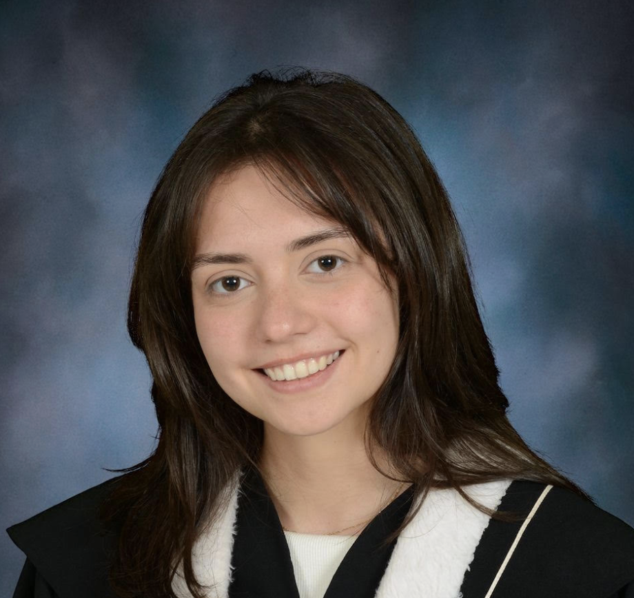 A young woman with shoulder-length brown hair wearing a black graduation gown with white trim, smiling against a blue and gray mottled background.