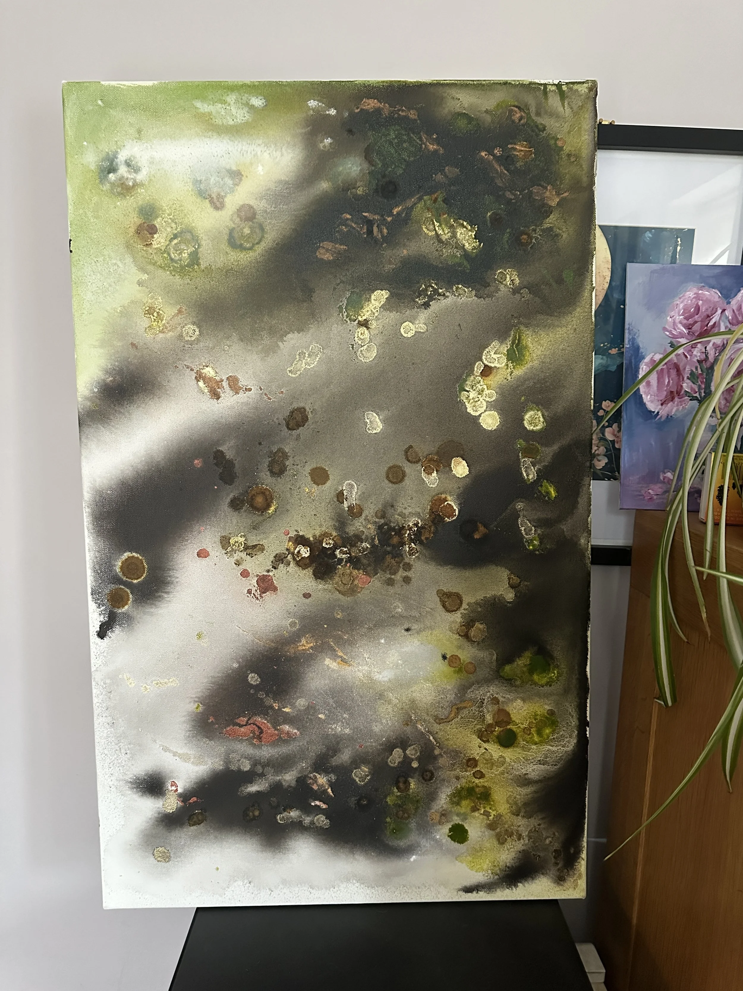 An abstract painting with green, black, white, and gold splashes and spots, displayed on a wall.