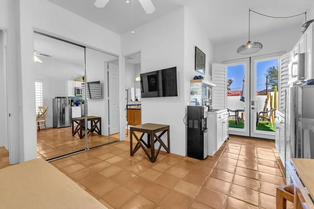 Open kitchen and dining area with white cabinets, a sliding glass door leading to an outdoor patio, and a view of a backyard with outdoor furniture and a palm tree.