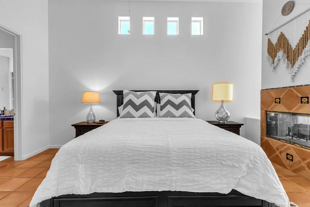 A bedroom with a bed, two nightstands with lamps, a fireplace, and decorative wall hanging