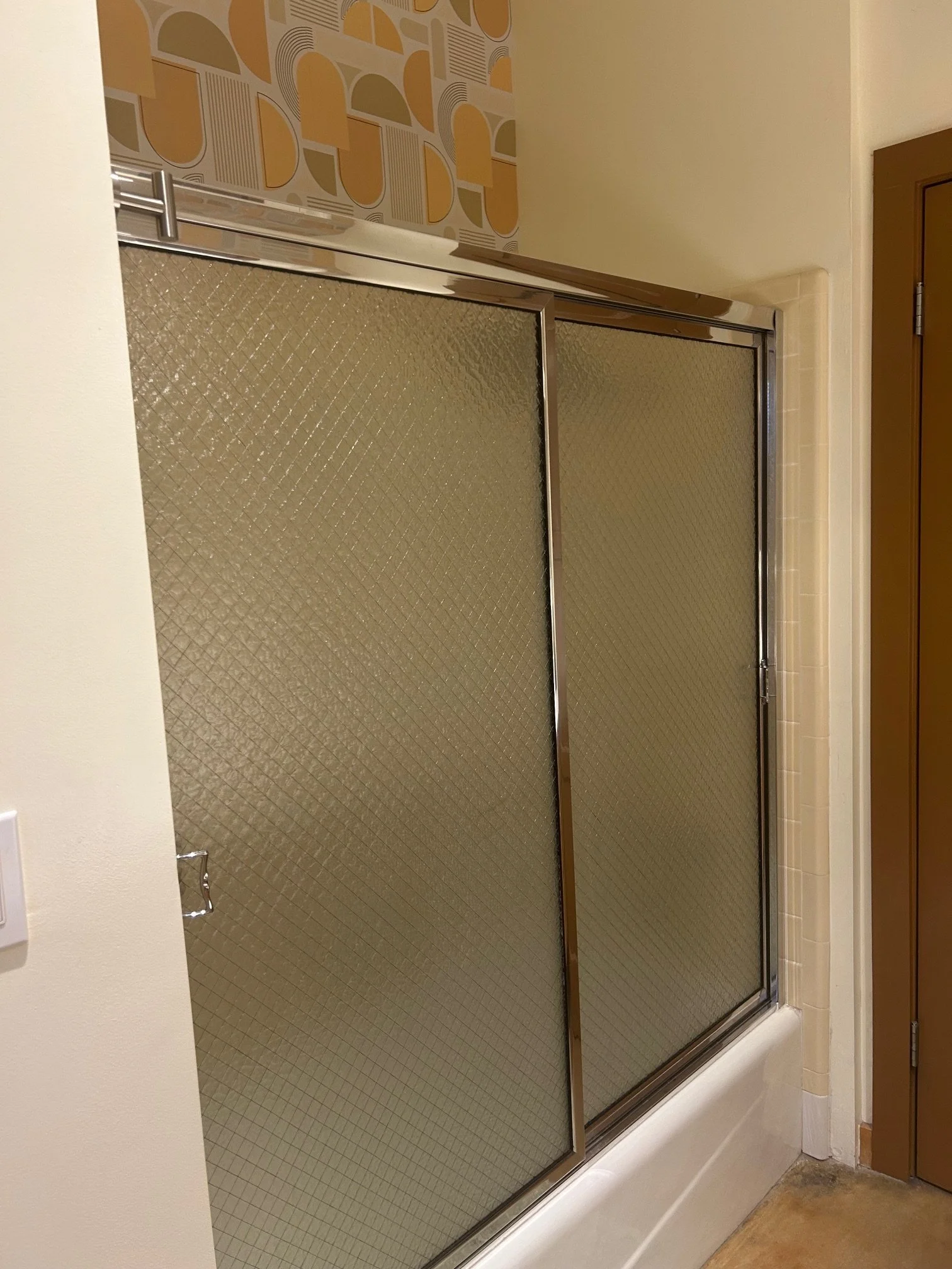 A bathroom shower with glass sliding doors, tiled interior, and a towel holder on the left wall.
