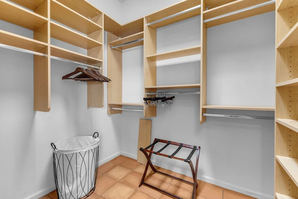 Empty walk-in closet with wooden shelves, hanging rods, a laundry basket, a luggage rack, and tile flooring.