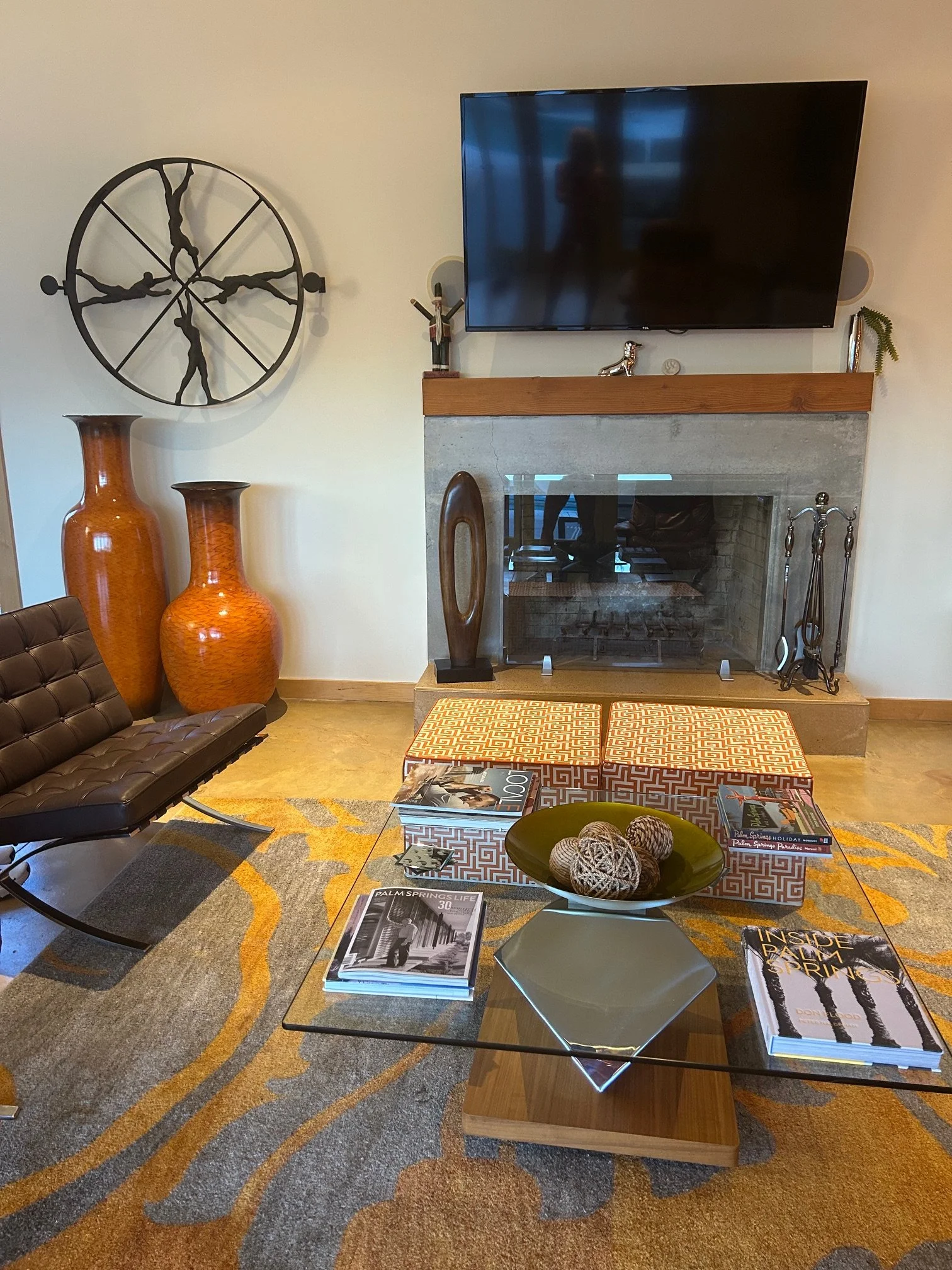 Living room with modern decor, featuring a fireplace, a flat-screen TV mounted on the wall, decorative vases, a coffee table with magazines and decorative objects, and chairs with patterned upholstery.