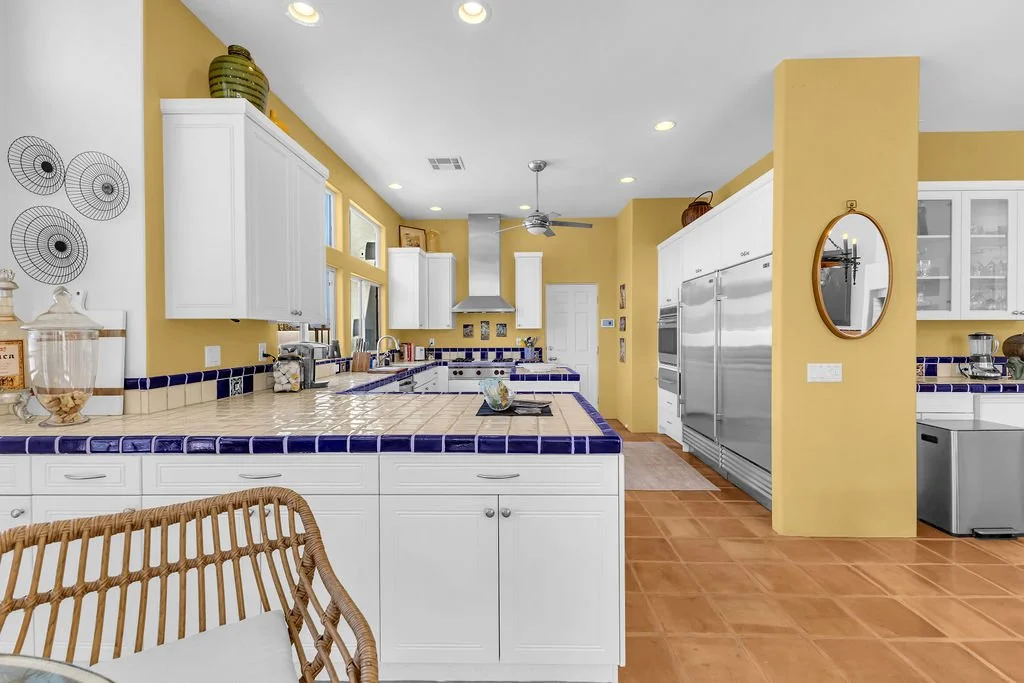 Bright kitchen with white cabinets, blue tiled countertops, yellow walls, and stainless steel appliances, including a double oven and refrigerator.