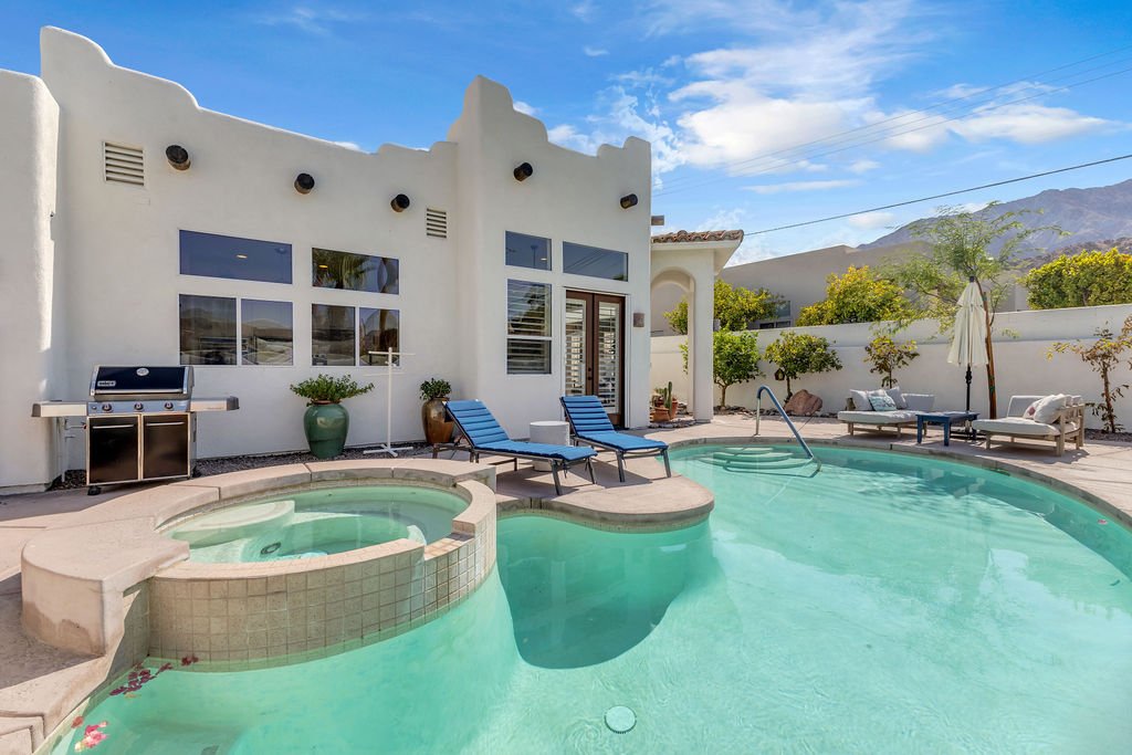Residential backyard with a swimming pool, hot tub, lounge chairs, and outdoor seating area.