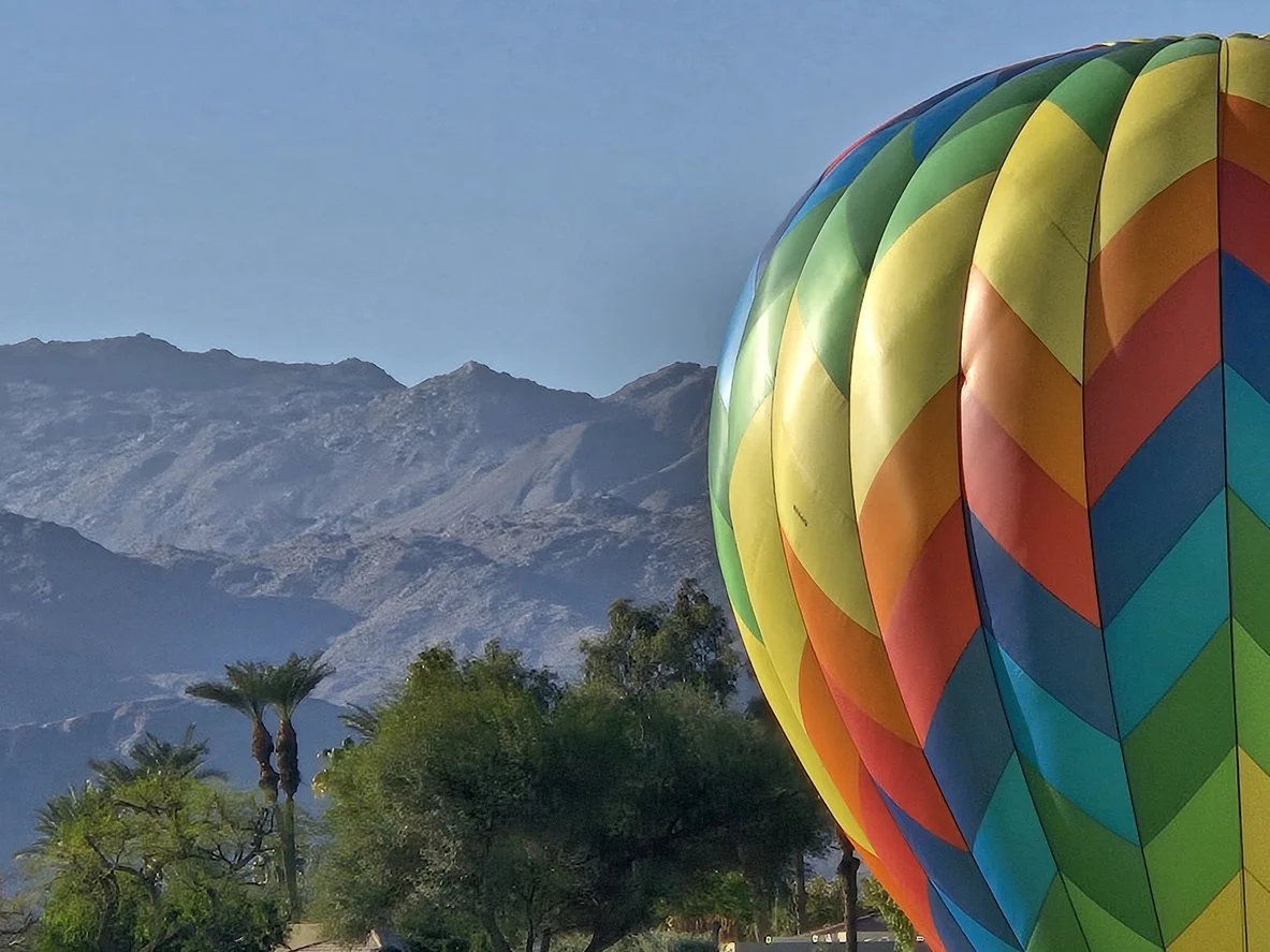 Colorful hot air balloon in the foreground with mountains and palm trees in the background.