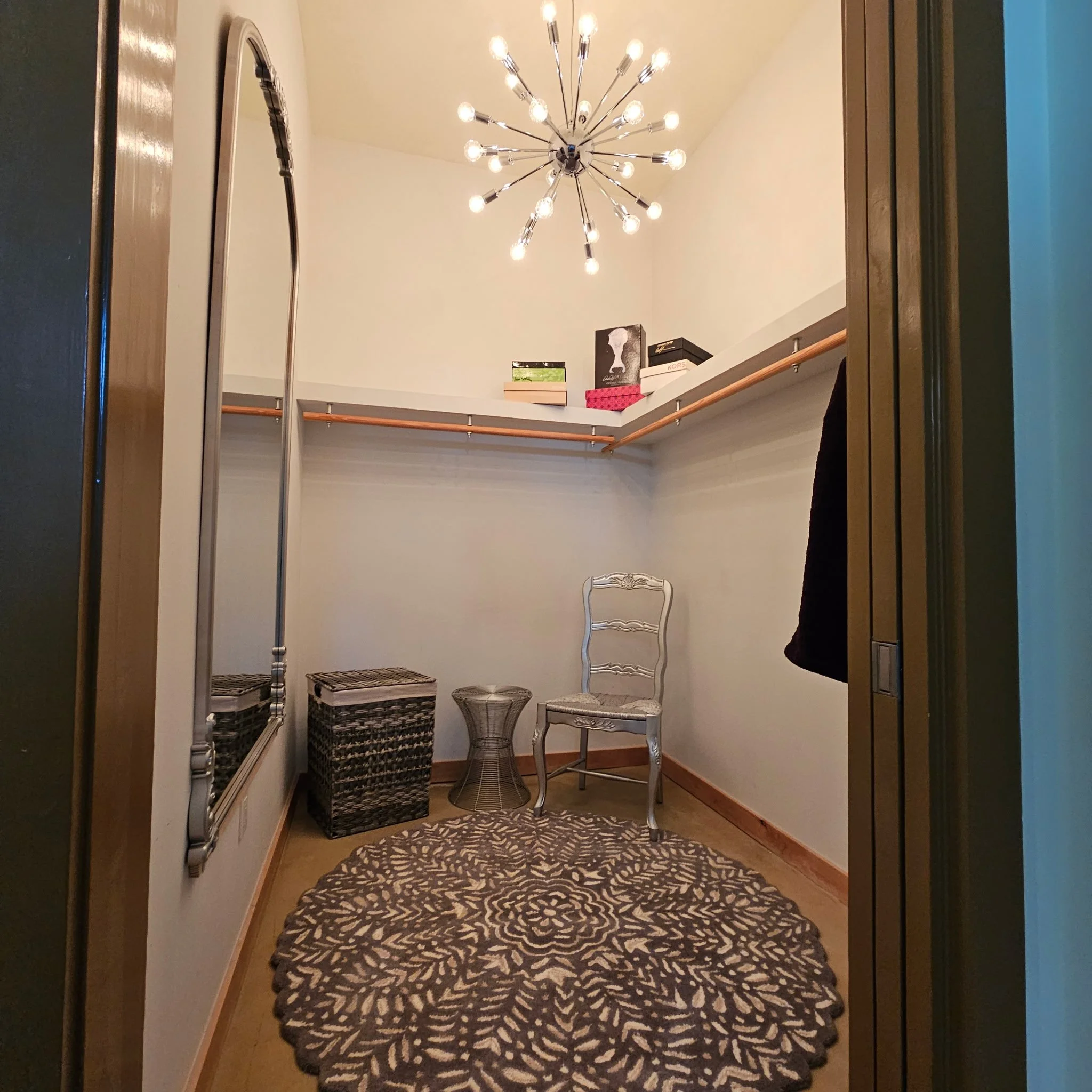 A small foyer with a rug with animal print, a white ornate chair, a tall wicker basket, and a chandelier hanging from the ceiling.