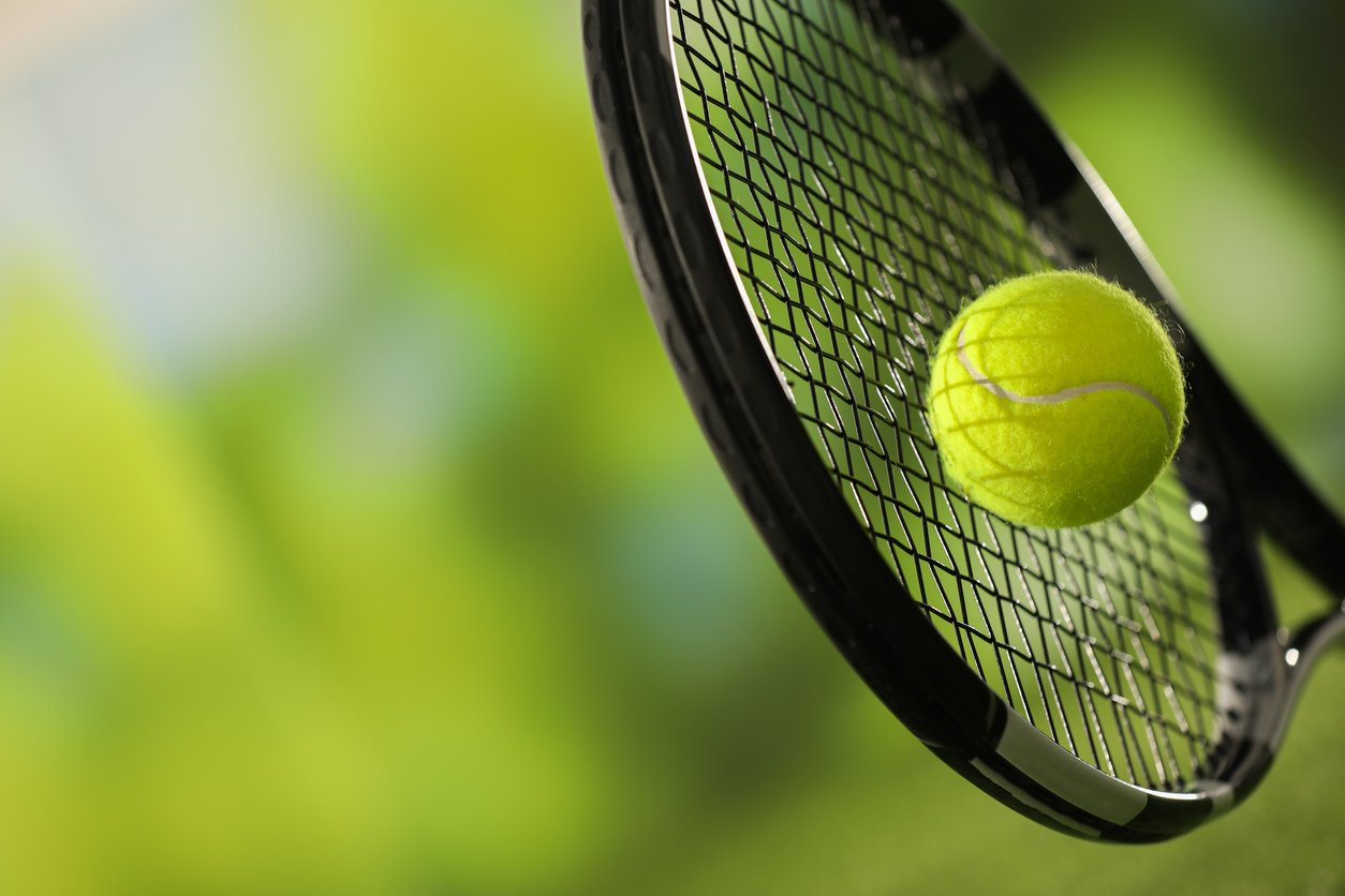 A yellow tennis ball on a tennis racket with a blurred green background.