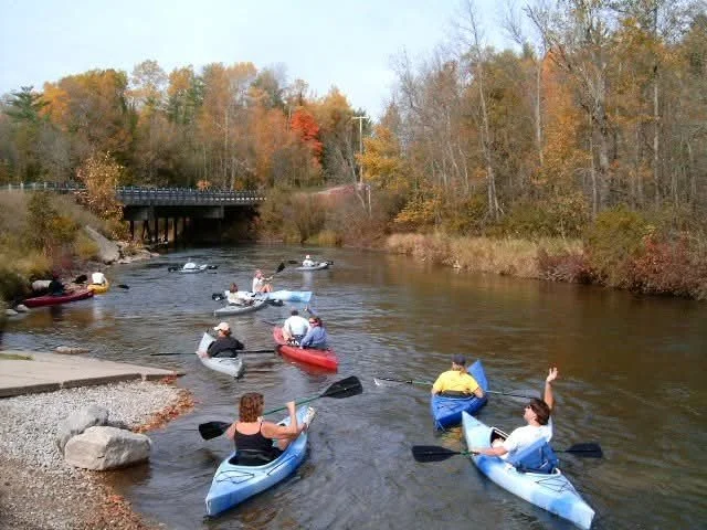 People kayaking and paddleboarding on a river surrounded by autumn trees.