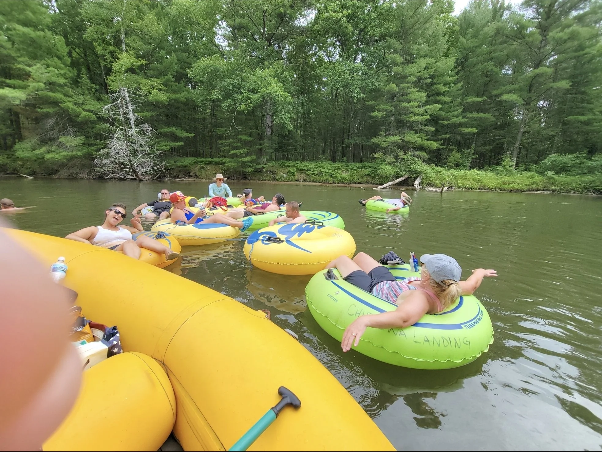 People floating on a river on colorful inflatable tubes, surrounded by green trees in a forested area.