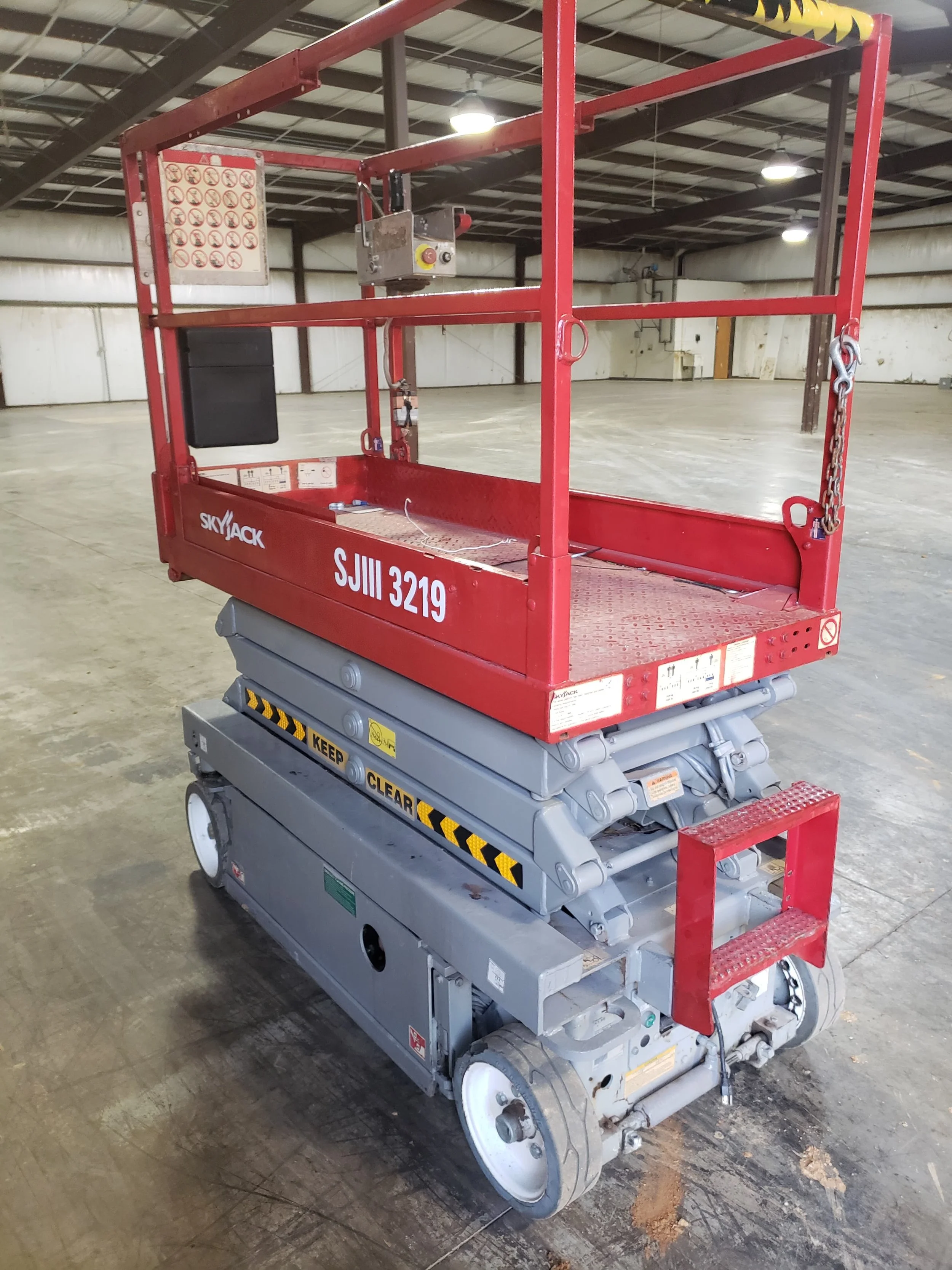 Empty red and gray construction lift in a large indoor warehouse with concrete floor and high metal ceiling.