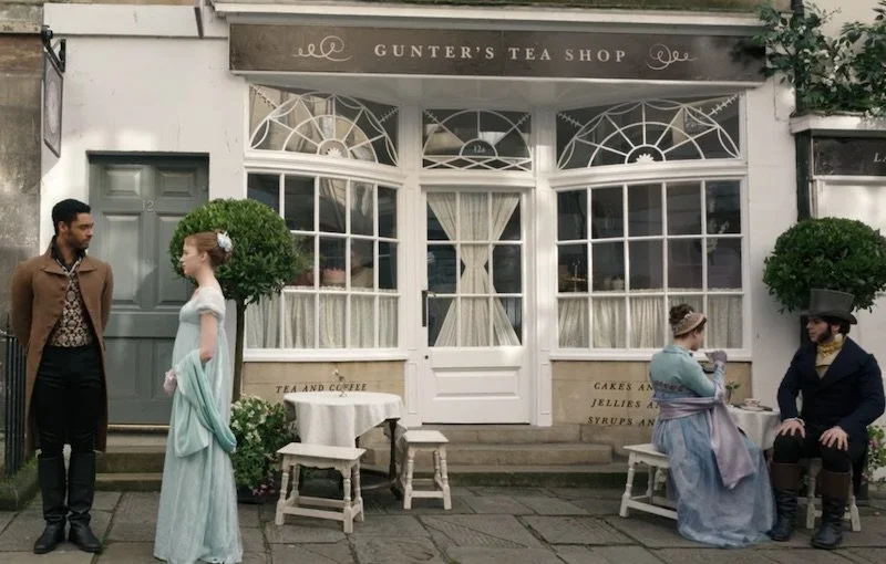People dressed in period costumes outside Gunter's Tea Shop, with two women and two men, and outdoor tables.