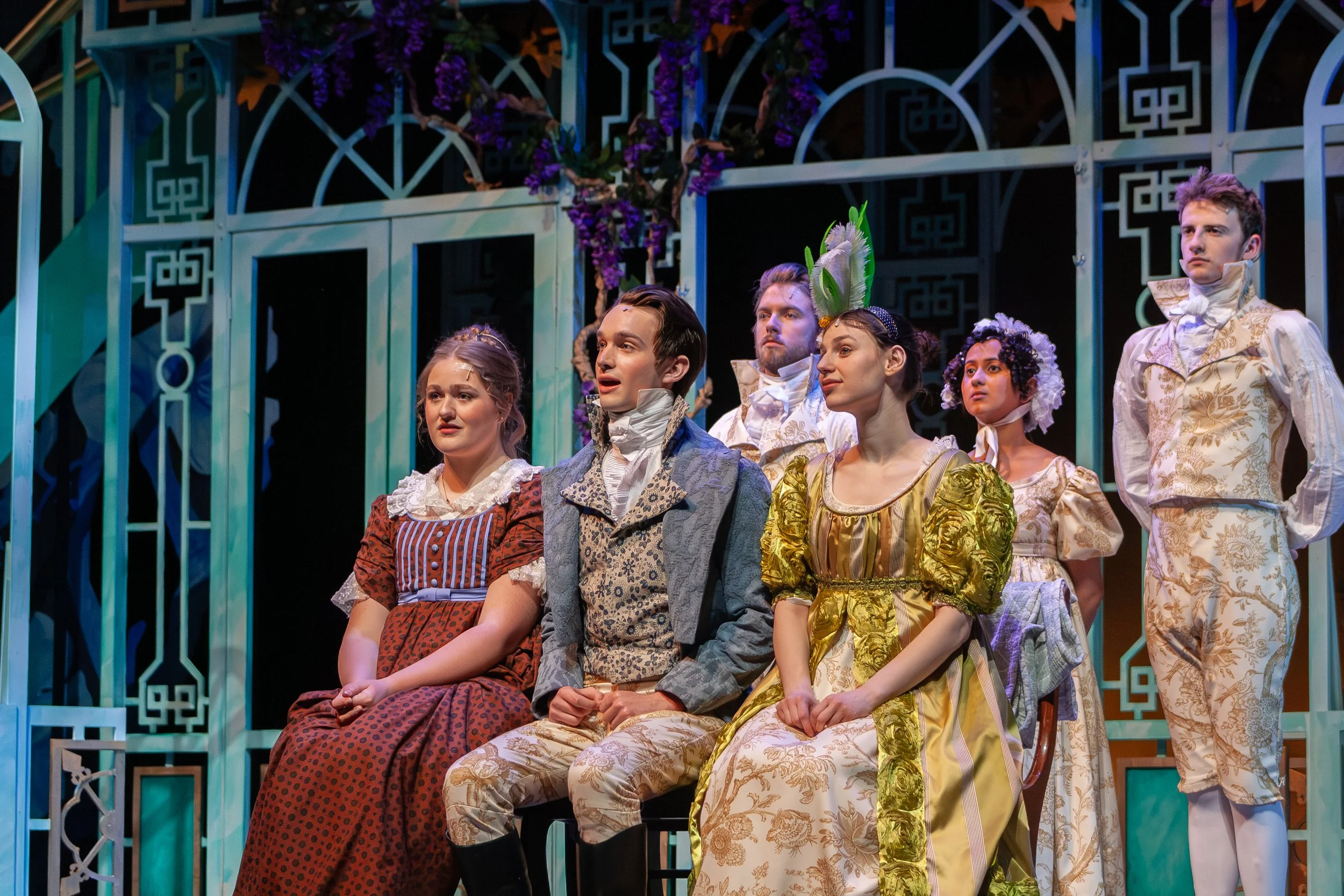 Group of actors in period costumes on stage during a theatrical performance.