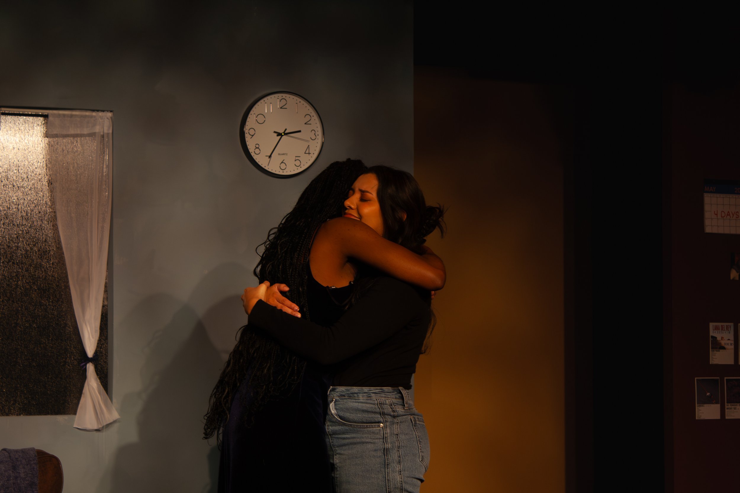 Two women hugging each other in a warm embrace, with a wall clock and a window in the background.