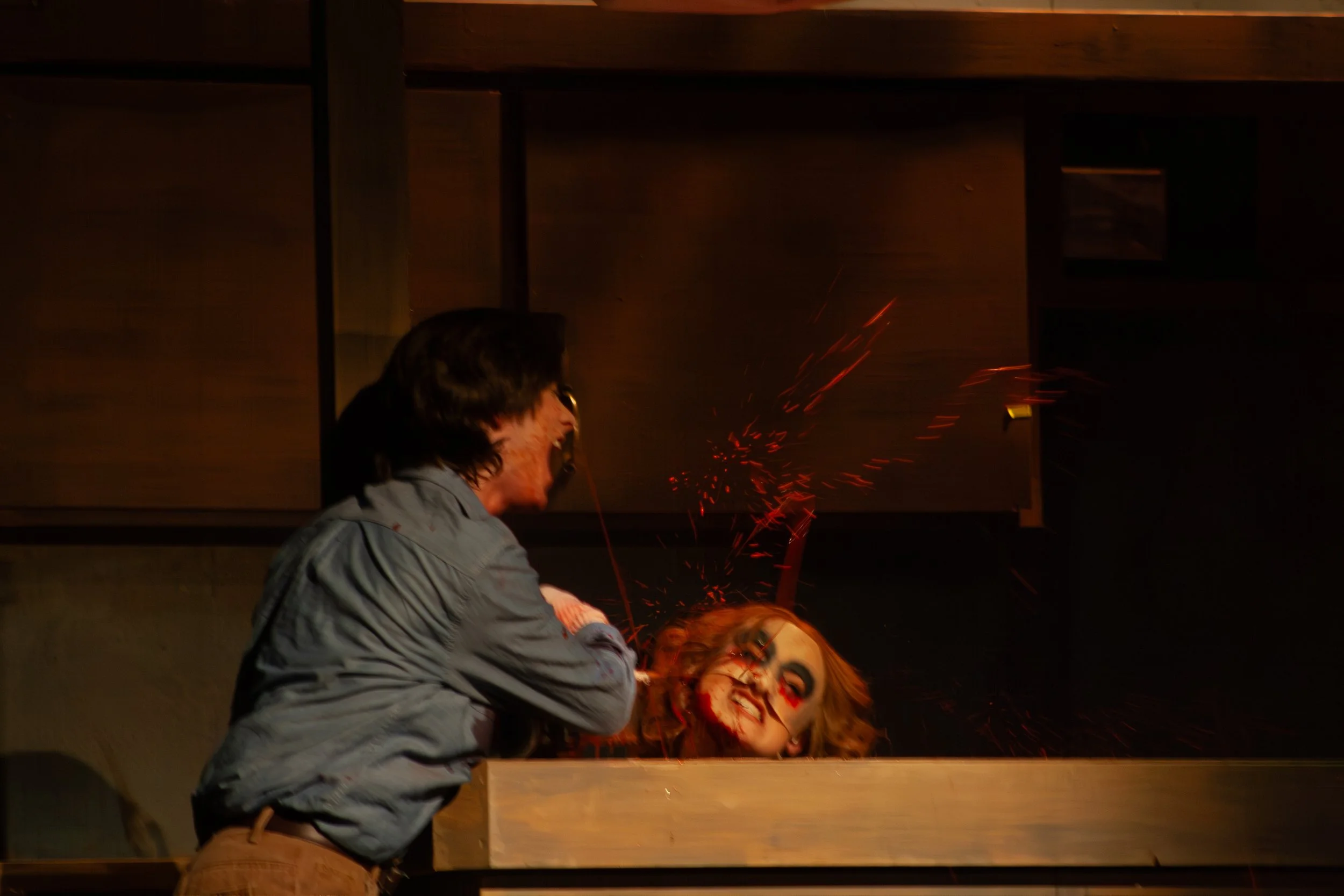 Two people are engaged in a dramatic scene involving blood and sparks. One person appears to be attacking or threatening the other, who is on the ground, looking distressed. The scene is intense and likely staged, with a dark background and minimal l