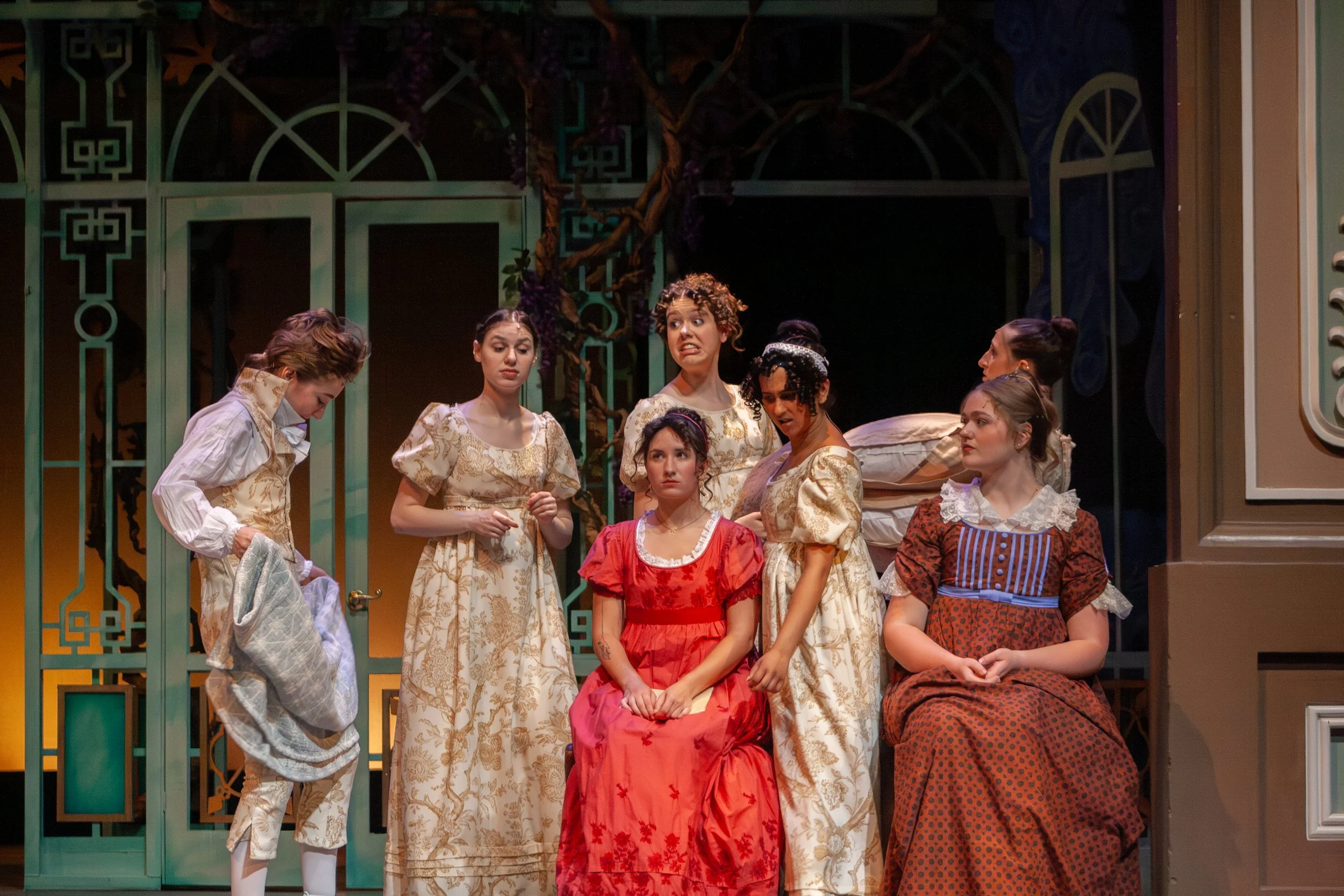 Actors dressed in historical costumes on a stage, with a green decorative backdrop, engaged in a theatrical performance.