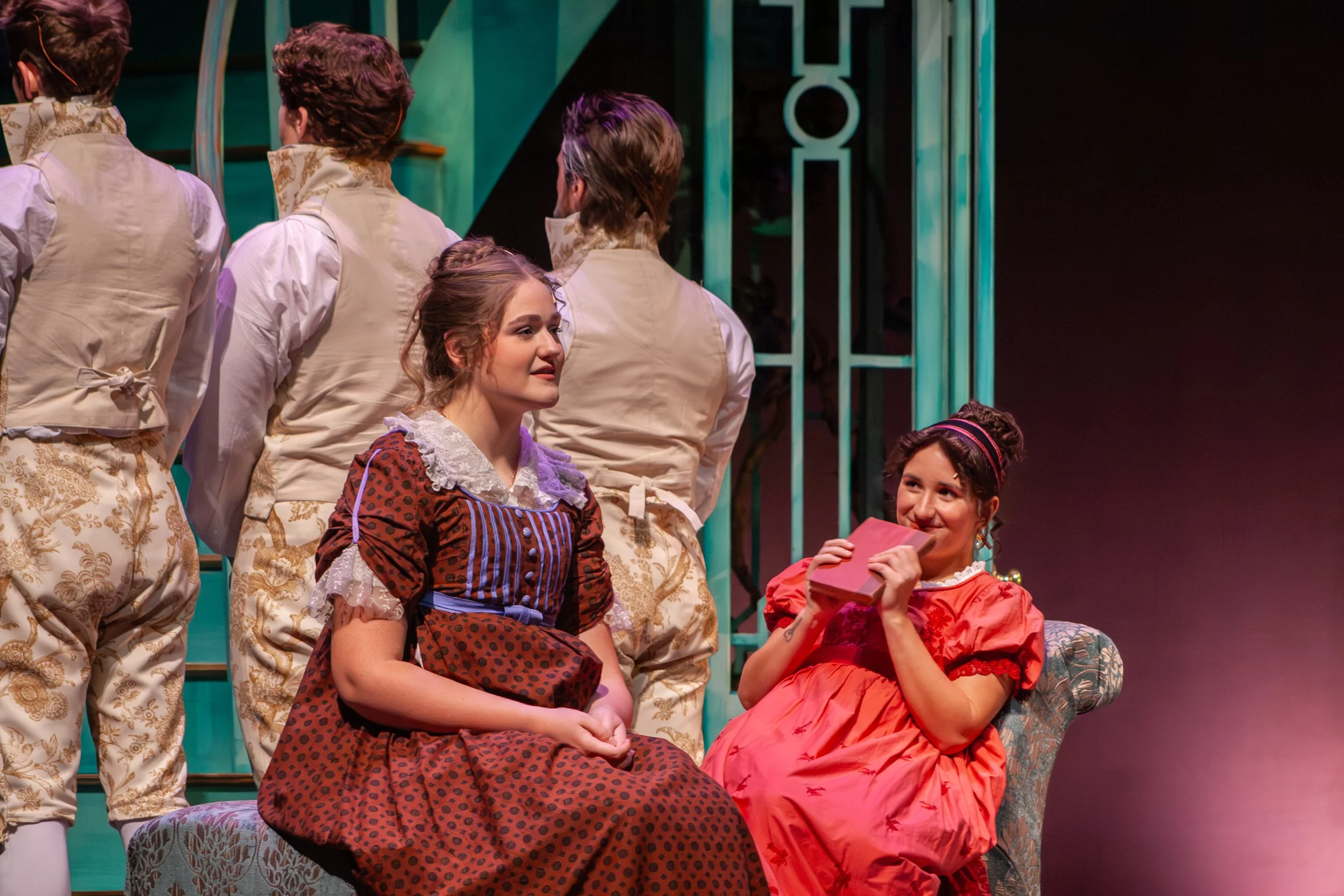 People dressed in vintage costumes on stage, some sitting and some standing, with a set featuring teal-colored bars and dark background.