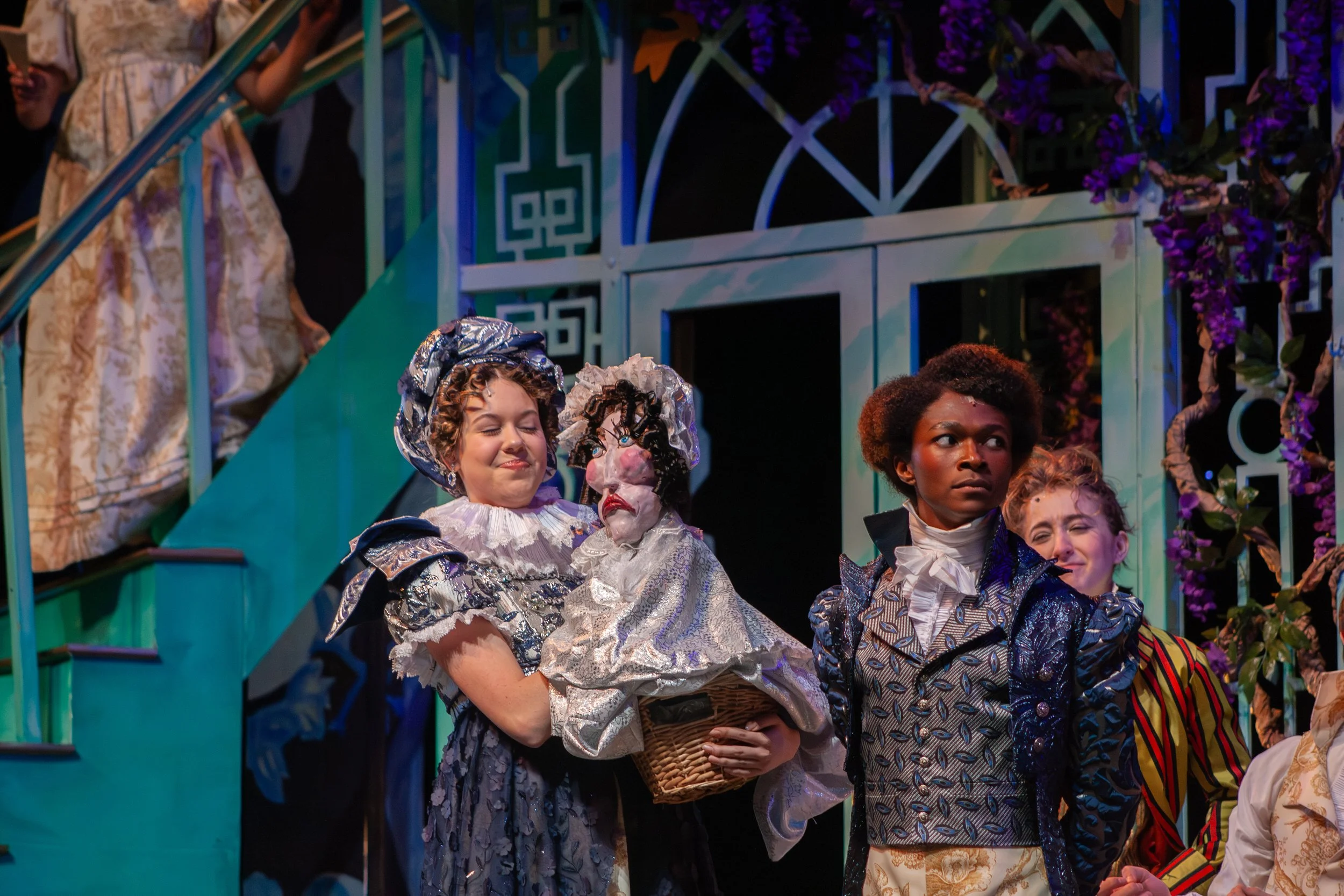 Actors on stage dressed as characters from 'The Wizard of Oz,' including a character with a pumpkin head and others in elaborate costumes, with a colorful set background.