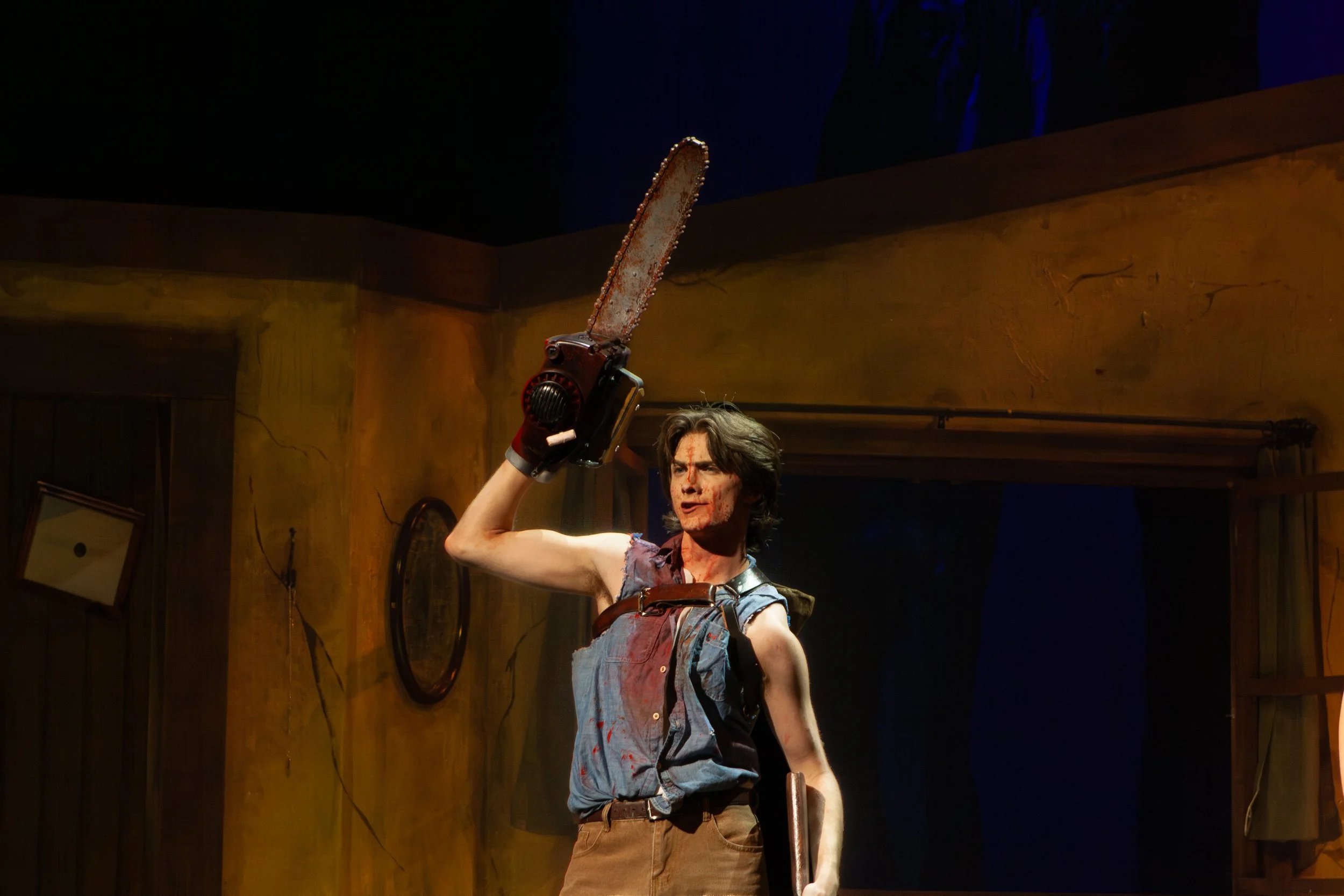 A man with long hair and bloody face holding a chainsaw.