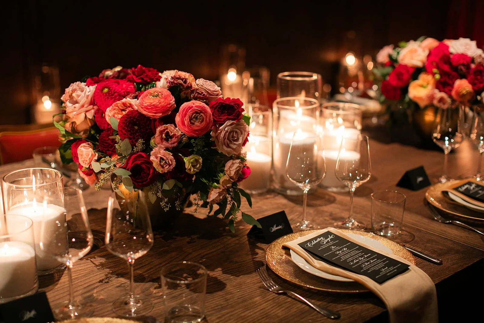 Elegant table setting with floral centerpiece, candles, wine glasses, and a menu card on a wooden table for a formal celebration.
