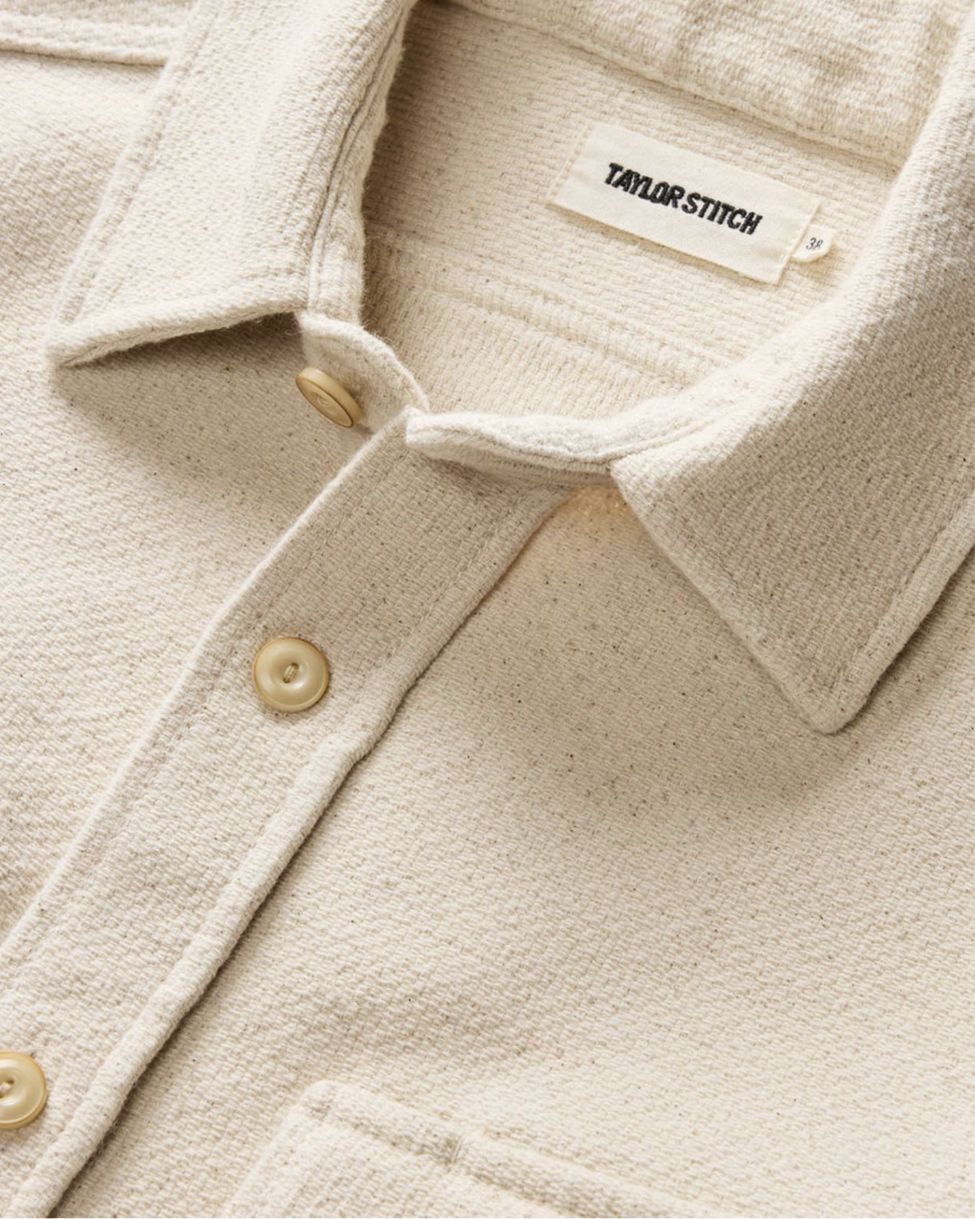Close-up of a beige, textured, button-up cardigan with cream-colored buttons and a brand label that reads "TAYLOR & STITCH."