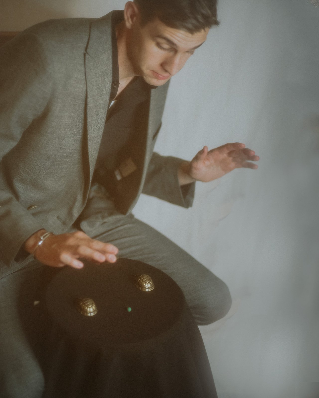 A man in a gray suit with a black shirt is sitting and moving three walnut shells and a pea around a table. The famous con game