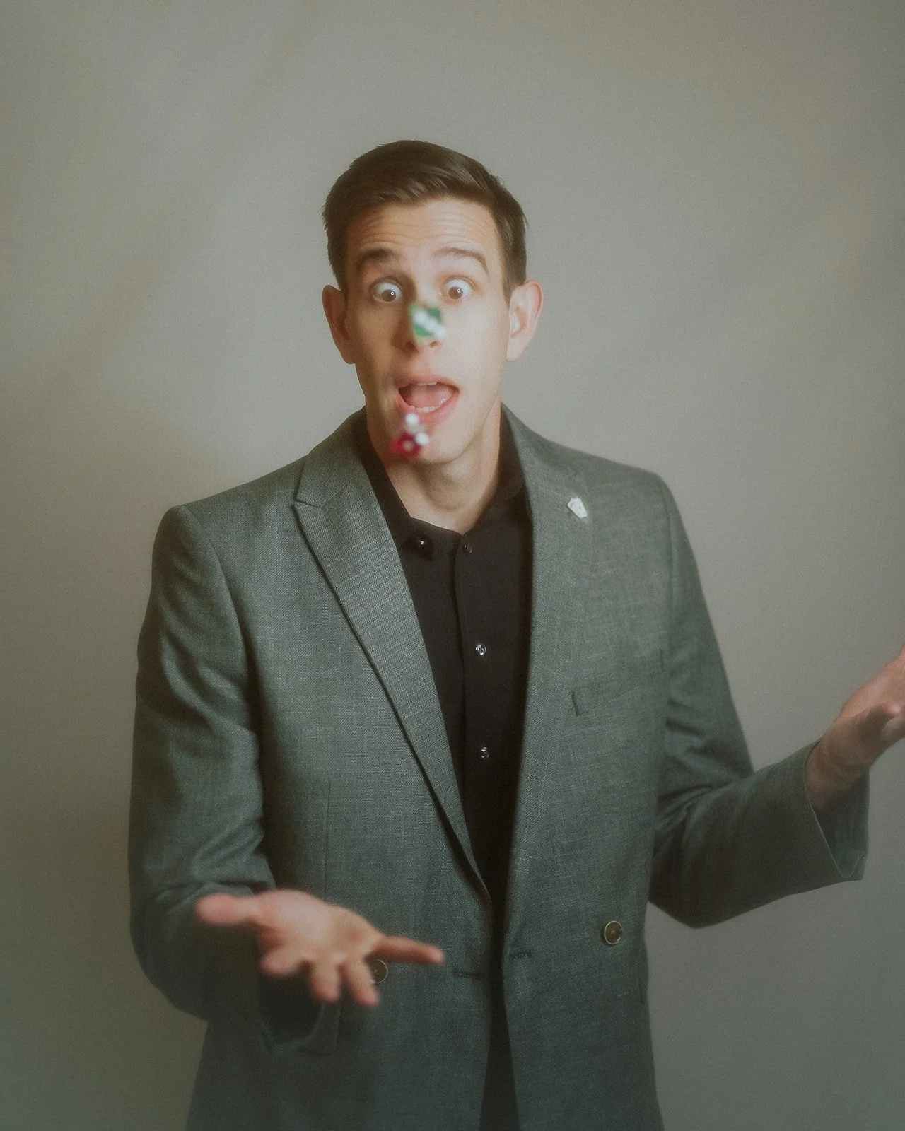 A man in a gray suit and black shirt with an excited expression throwing dice into the air