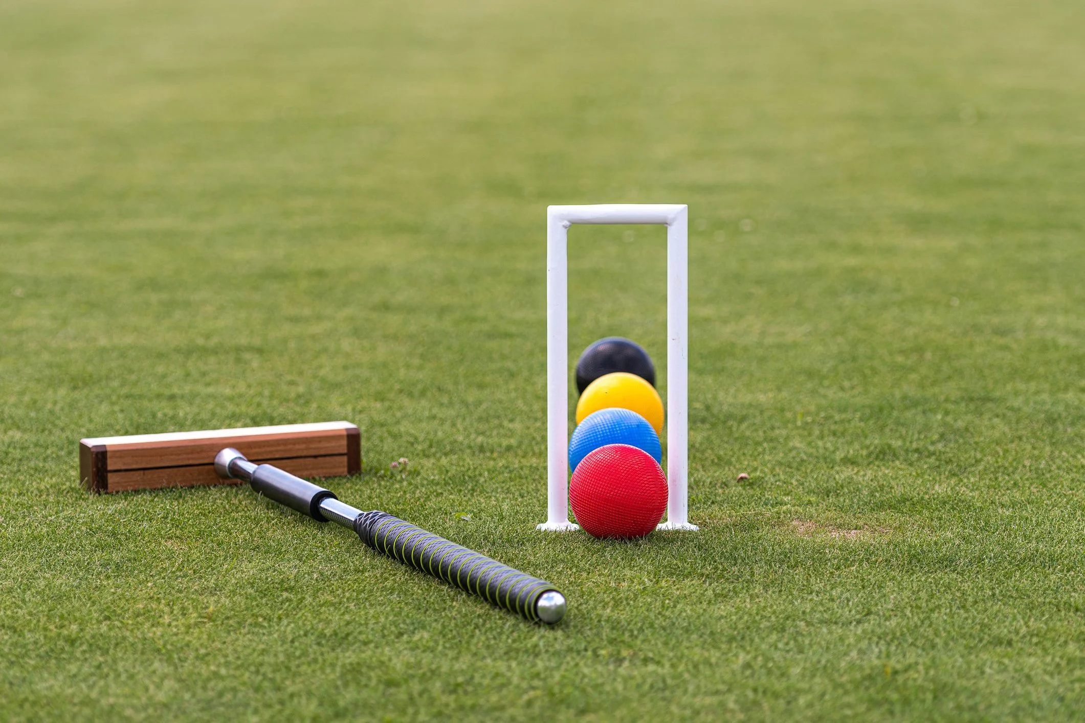 Golf training equipment arranged on a grassy field, including colored golf balls, a training frame, a wooden block, and a golf club.