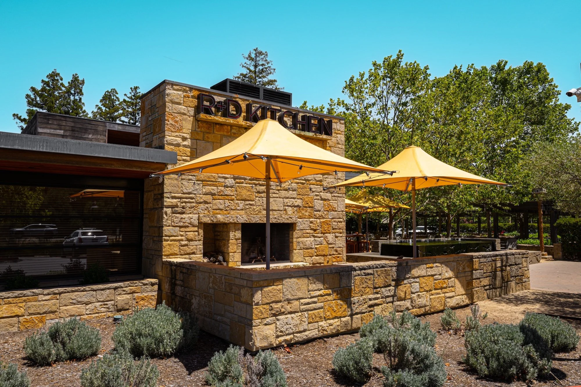 Exterior of a building with a stone facade, yellow umbrellas, and trees surrounding the area.