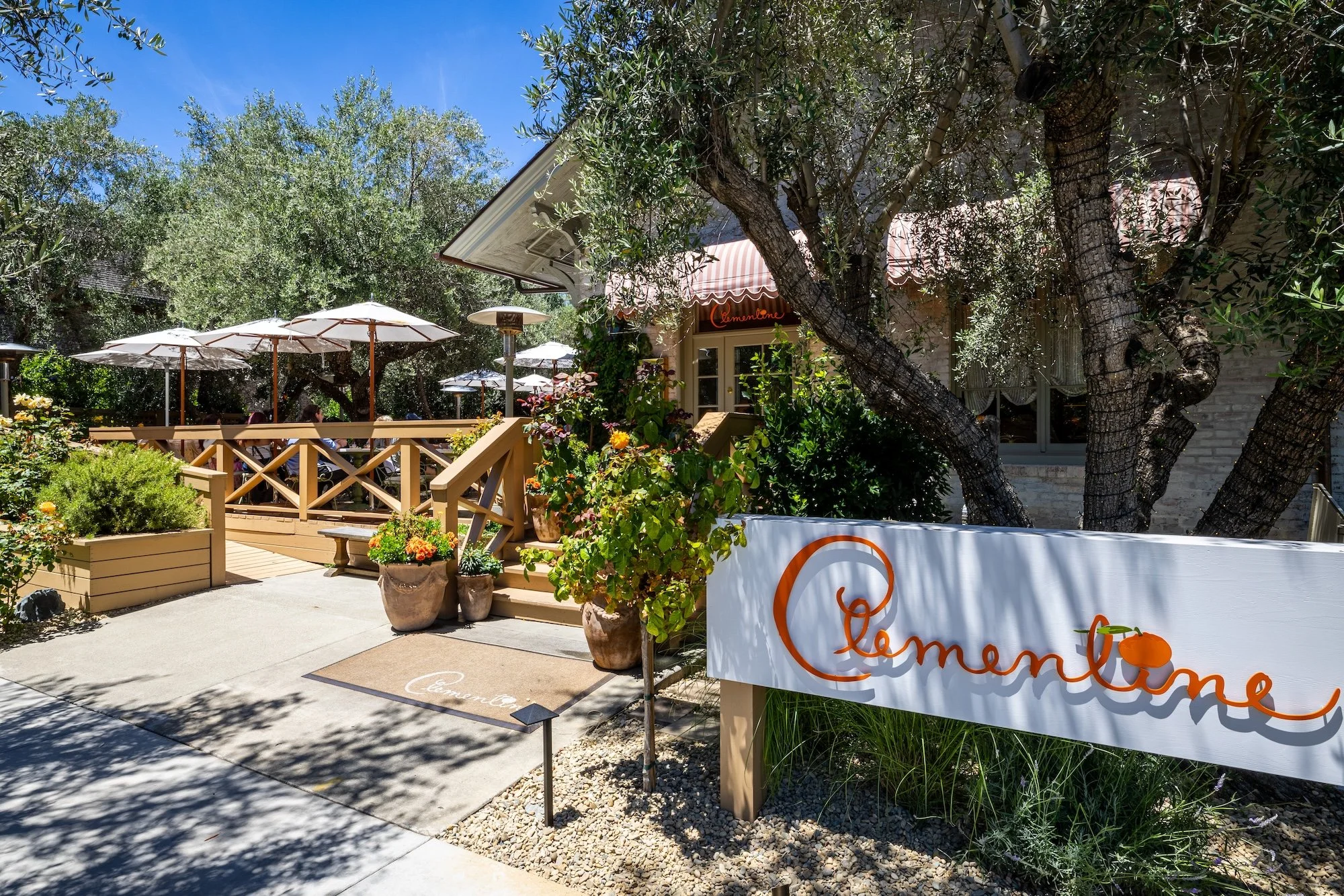 Outdoor patio of a restaurant with several white umbrellas, potted plants, and trees surrounding the seating area.