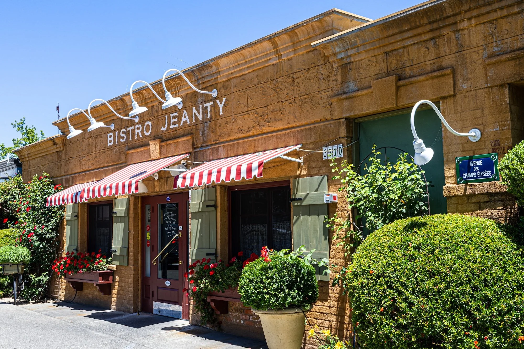 The exterior of Bistro Jeanty, a cozy restaurant with a brick facade, green shutters, and outdoor plants, located on Avenue des Champs Élysées.
