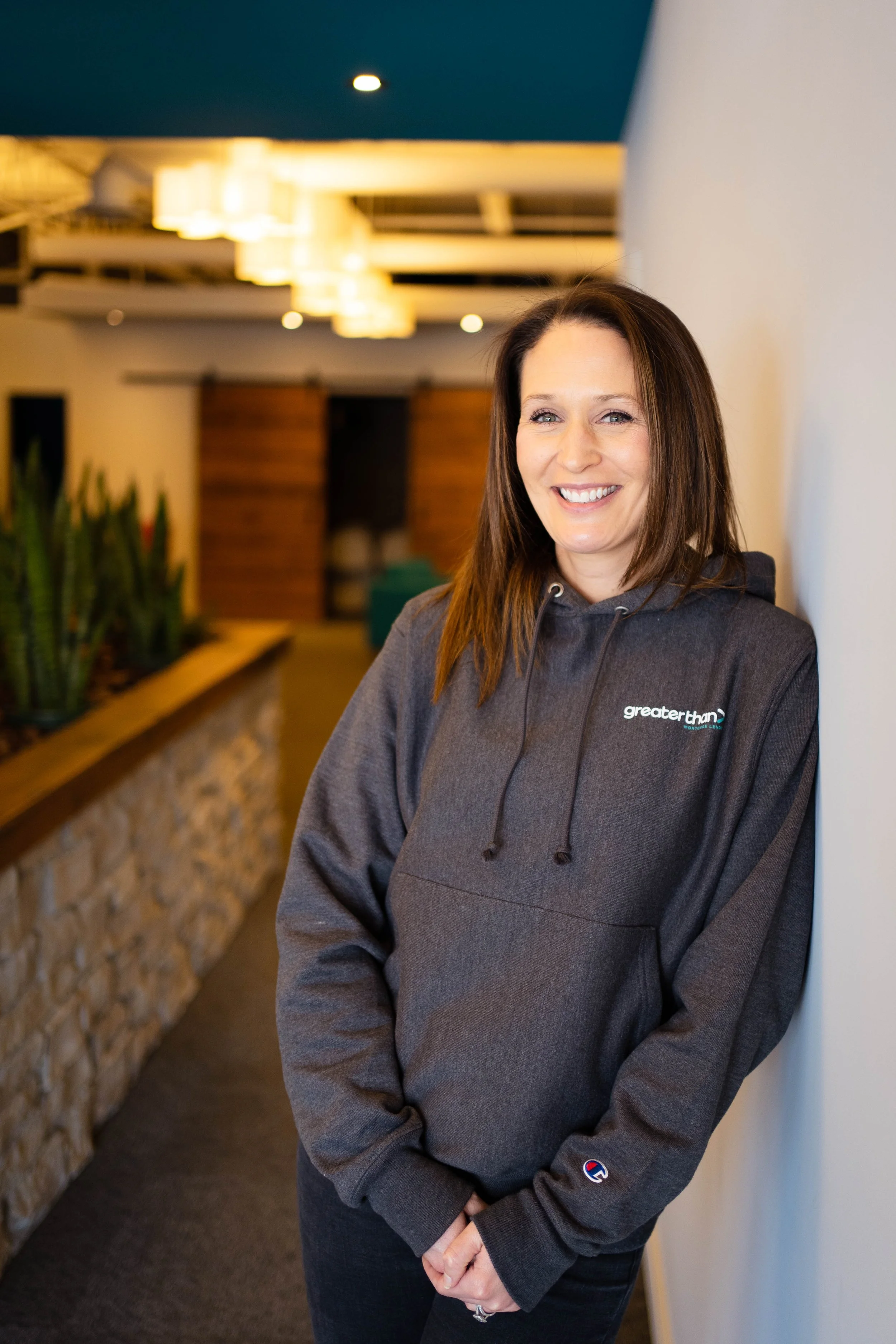 Kate in a gray hoodie leaning against a white wall in an office hallway.